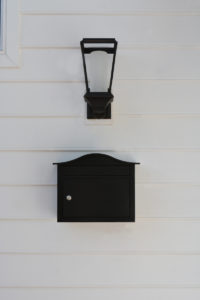 locking black wall mount mailbox installed on white siding