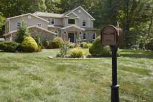 Decorative brown mailbox on a lawn behind a house