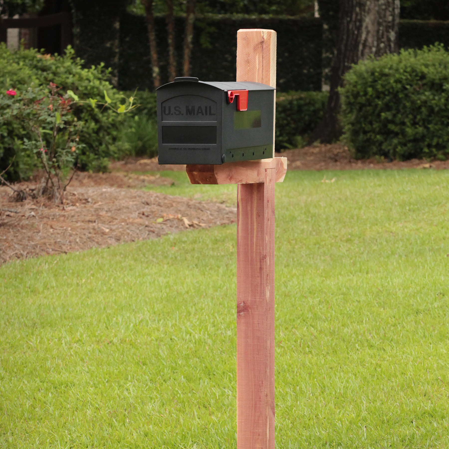 USPS mailbox mounted on a wooden post in a grassy yard with a red flag visible
