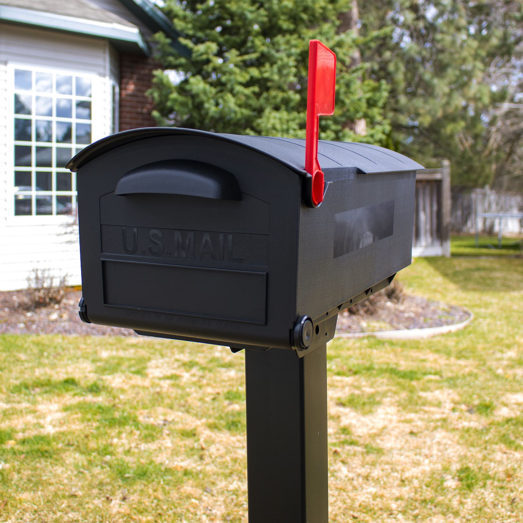 Black U.S. Mail mailbox with red flag raised on a post in a residential yard.
