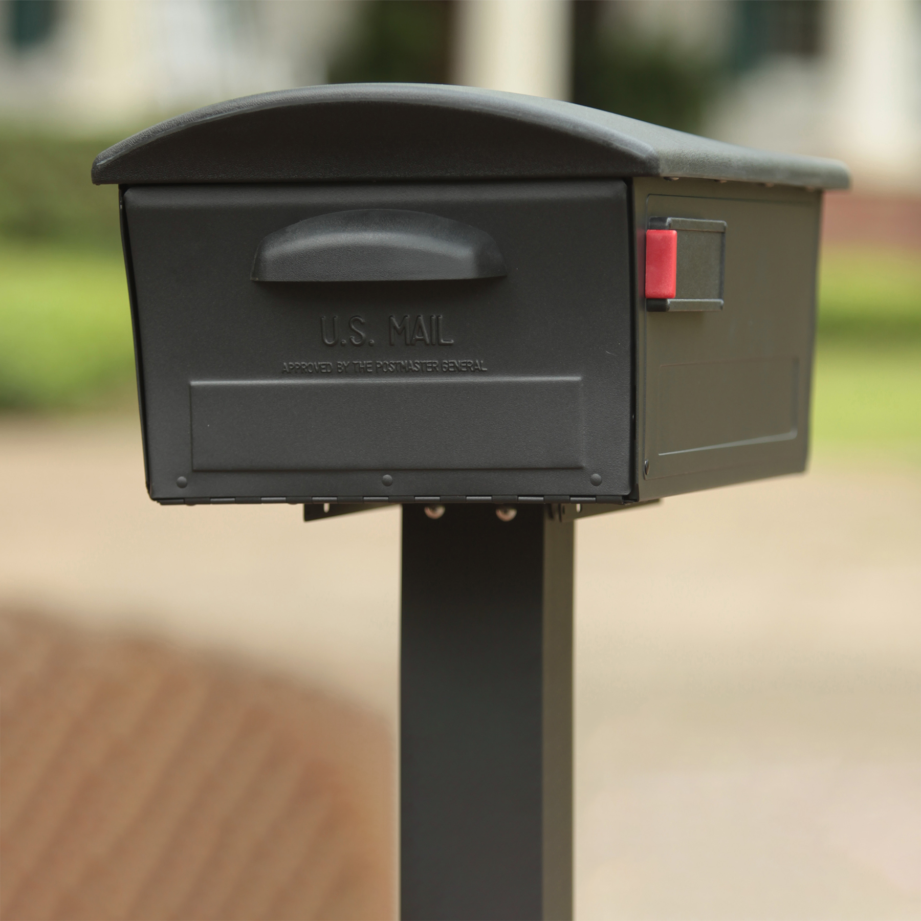 Black USPS mailbox on a post with a raised red flag in a suburban setting