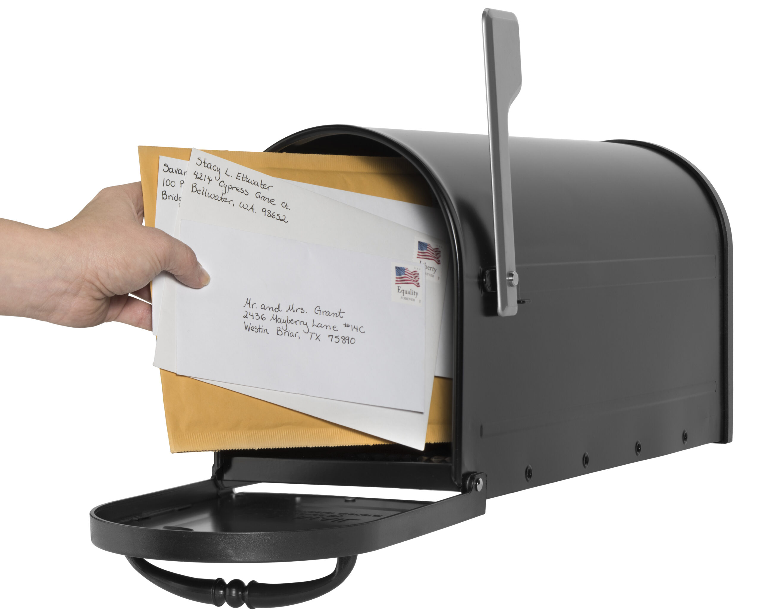 Hand inserting letters into a black curbside mailbox outside.