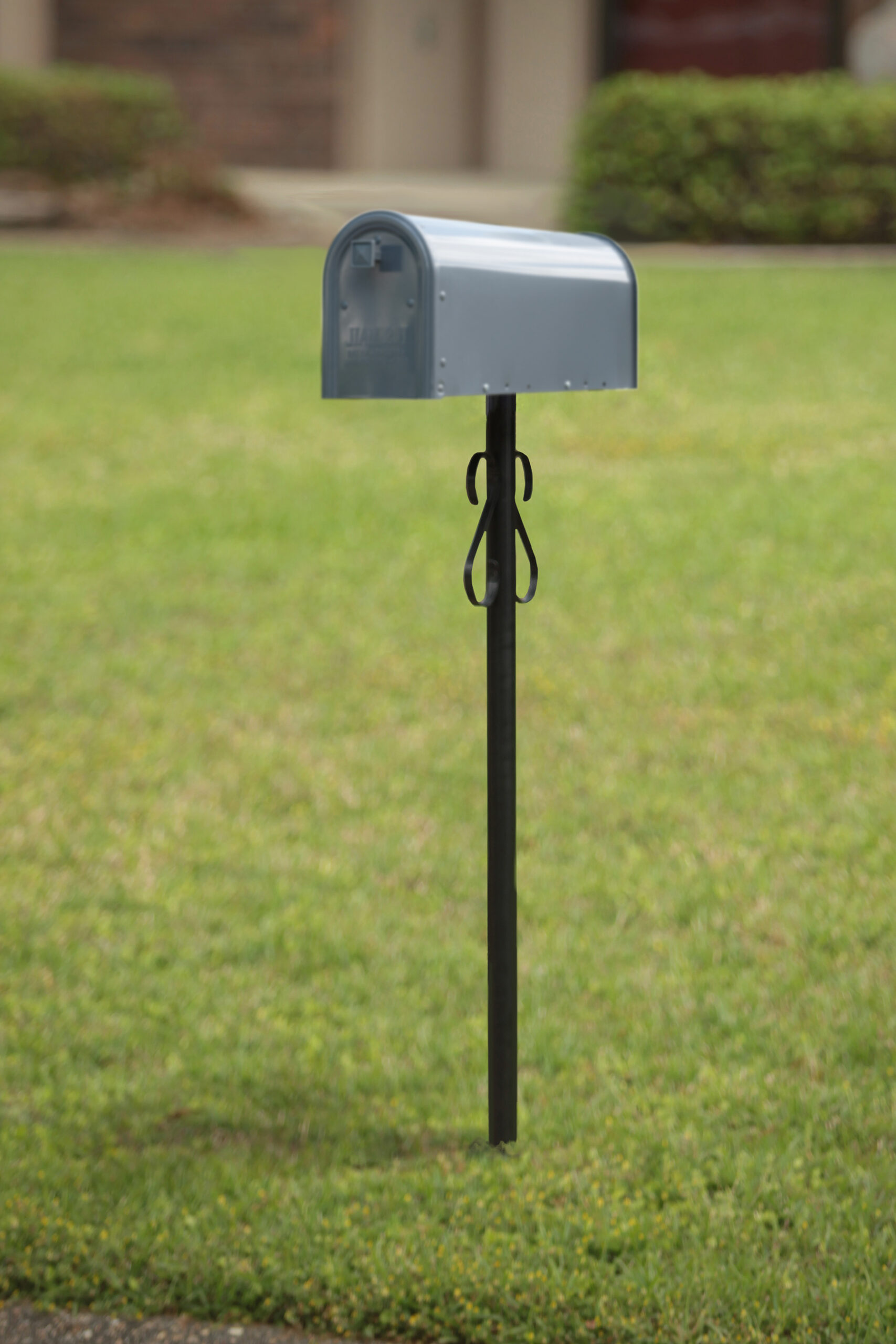 Gray curved-top mailbox mounted on a black post in a grassy front yard.