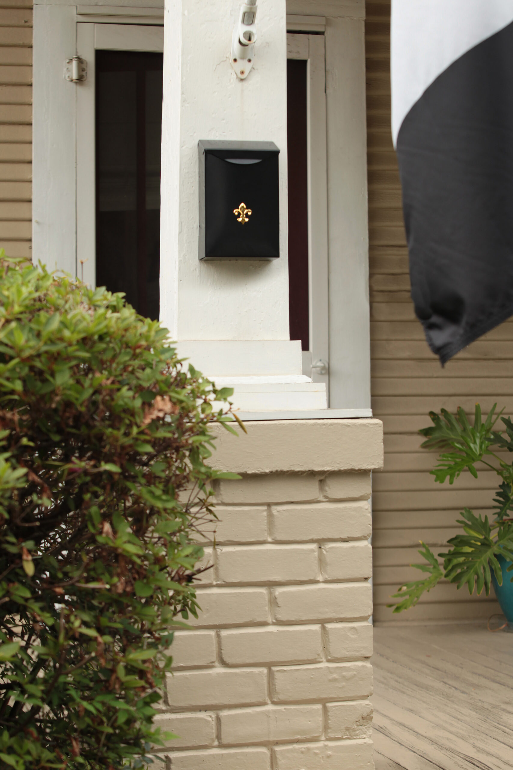 Black wall mailbox with a gold fleur-de-lis on a white porch column