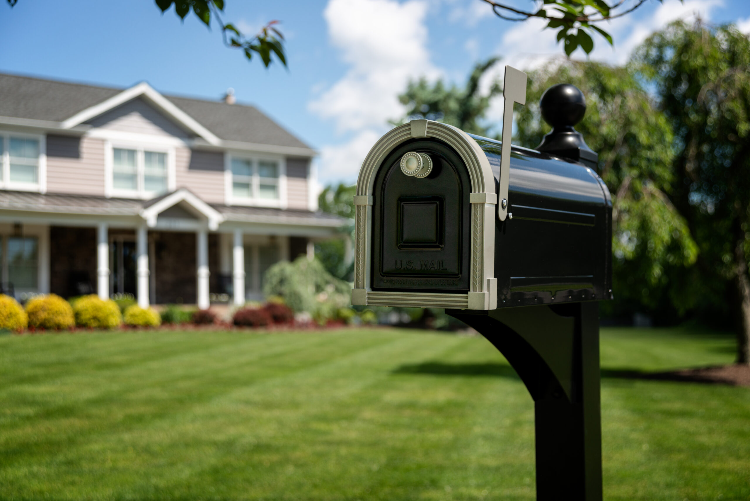 Mailbox with raised flag in the foreground of a well-kept front yard.