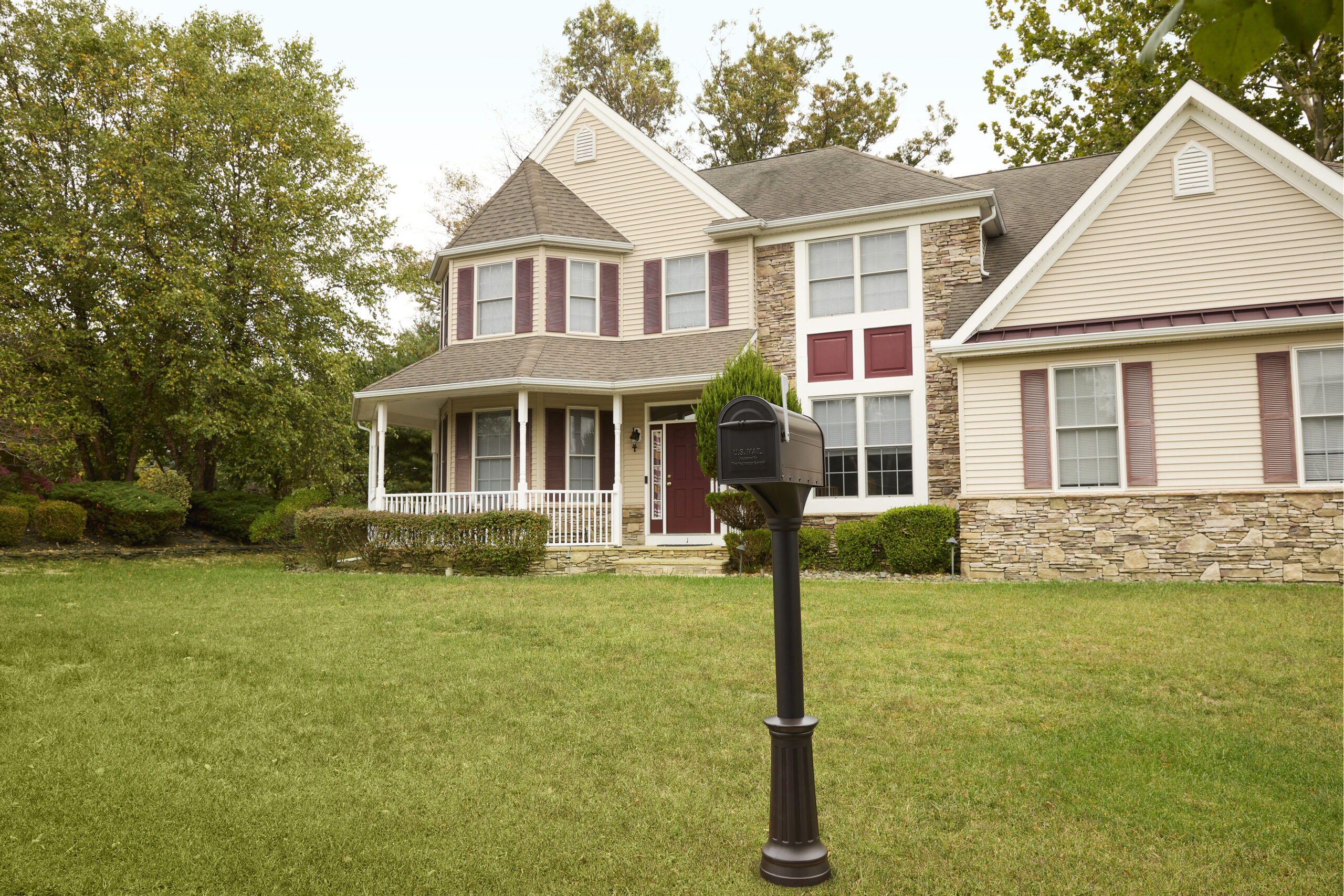 Two-story suburban house with beige siding, stone accents, burgundy shutters, and a covered front porch, seen from the yard with a black mailbox in the foreground.
