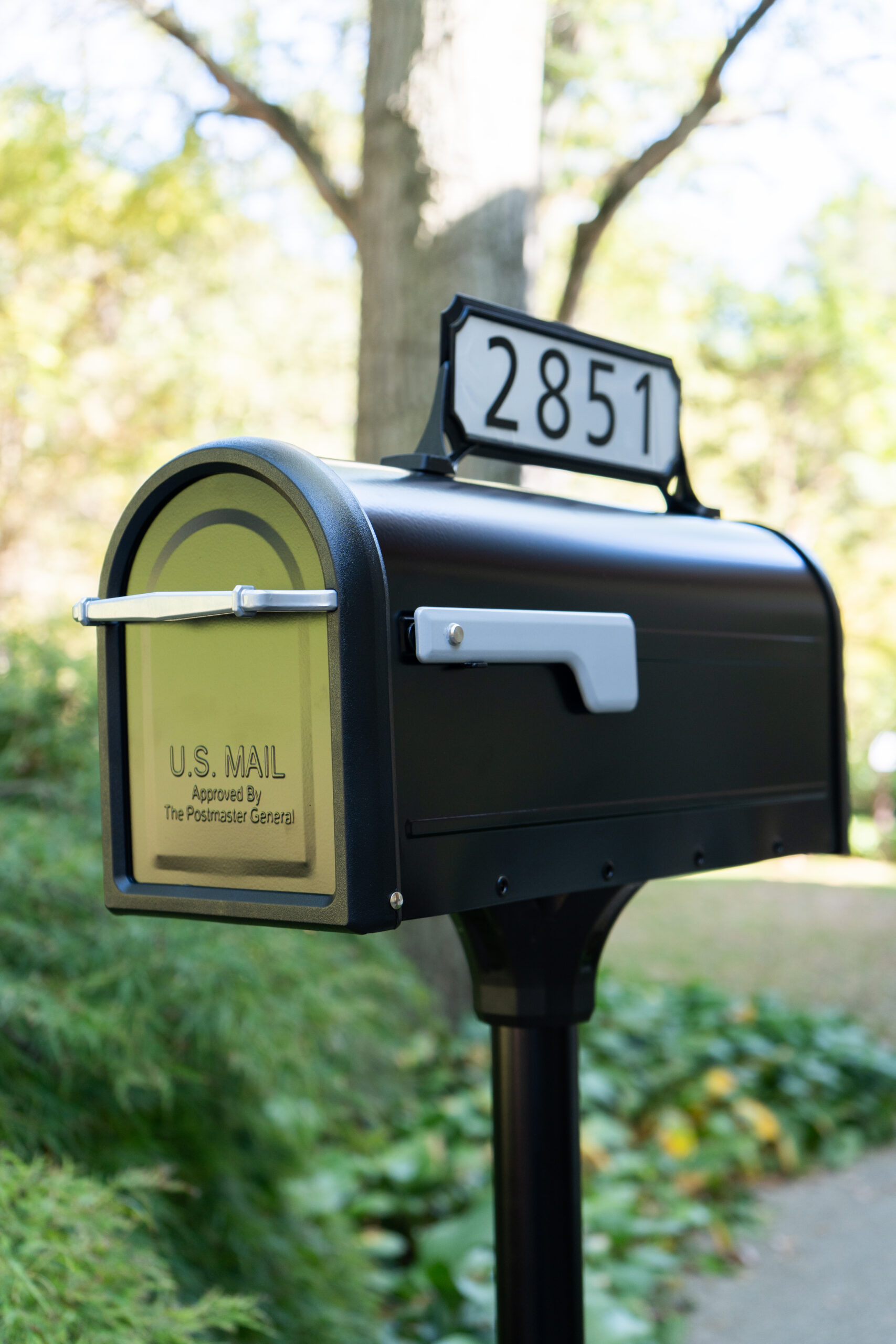 U.S. mail mailbox on a post with the number 2851 displayed on top in a suburban yard, ready for pickup or delivery.