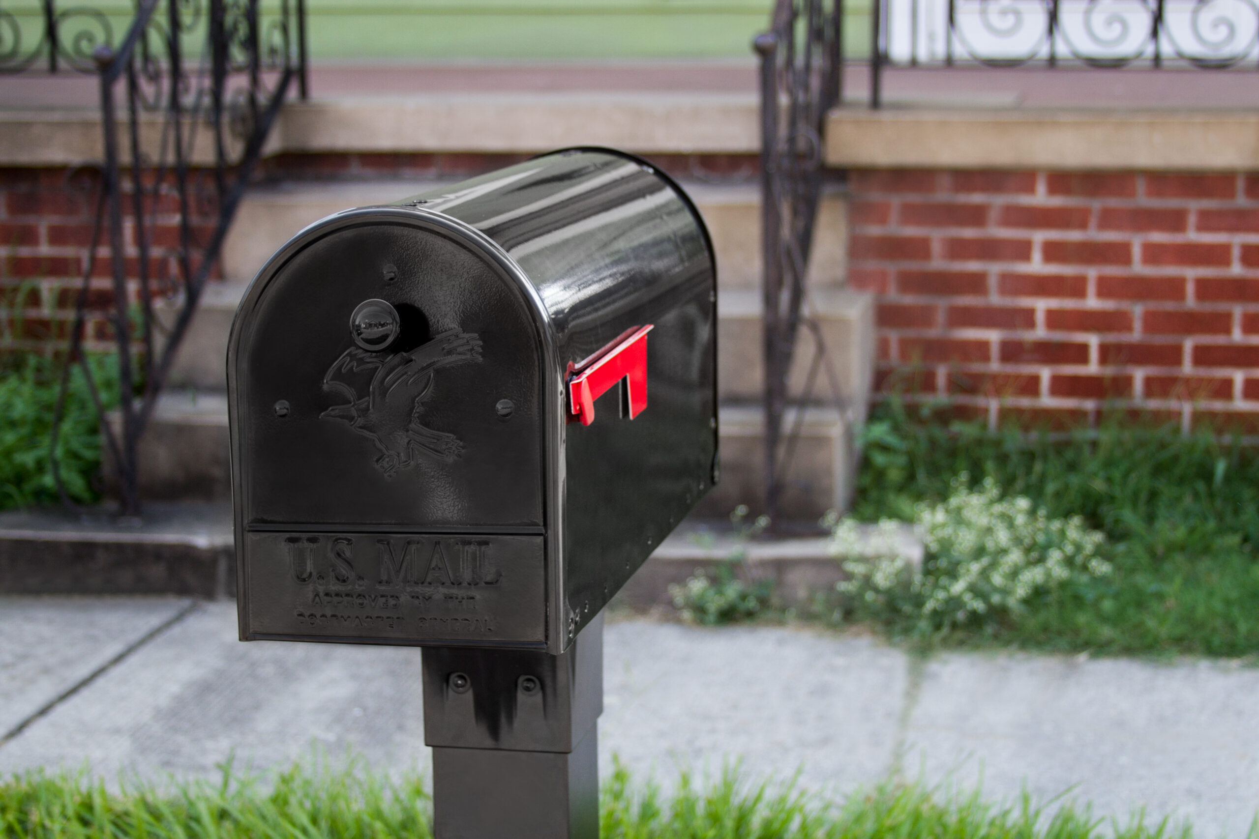 Black U.S. Mail mailbox with the red flag raised, in front of a brick porch.
