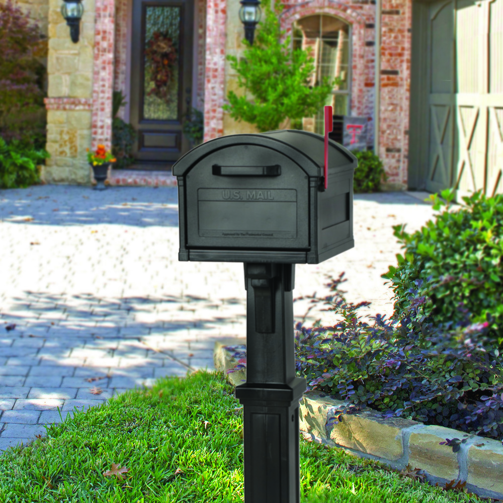 Black USPS mailbox on a post in a suburban front yard with a brick house and green lawn in the background.