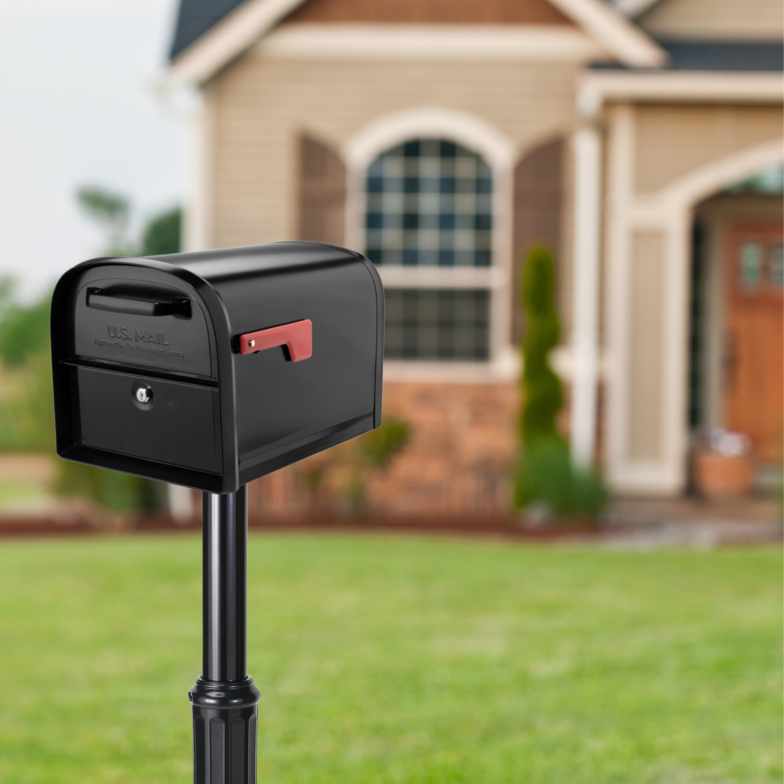 Black mailbox on a metal post in a front yard, with a red flag raised, in front of a suburban house.
