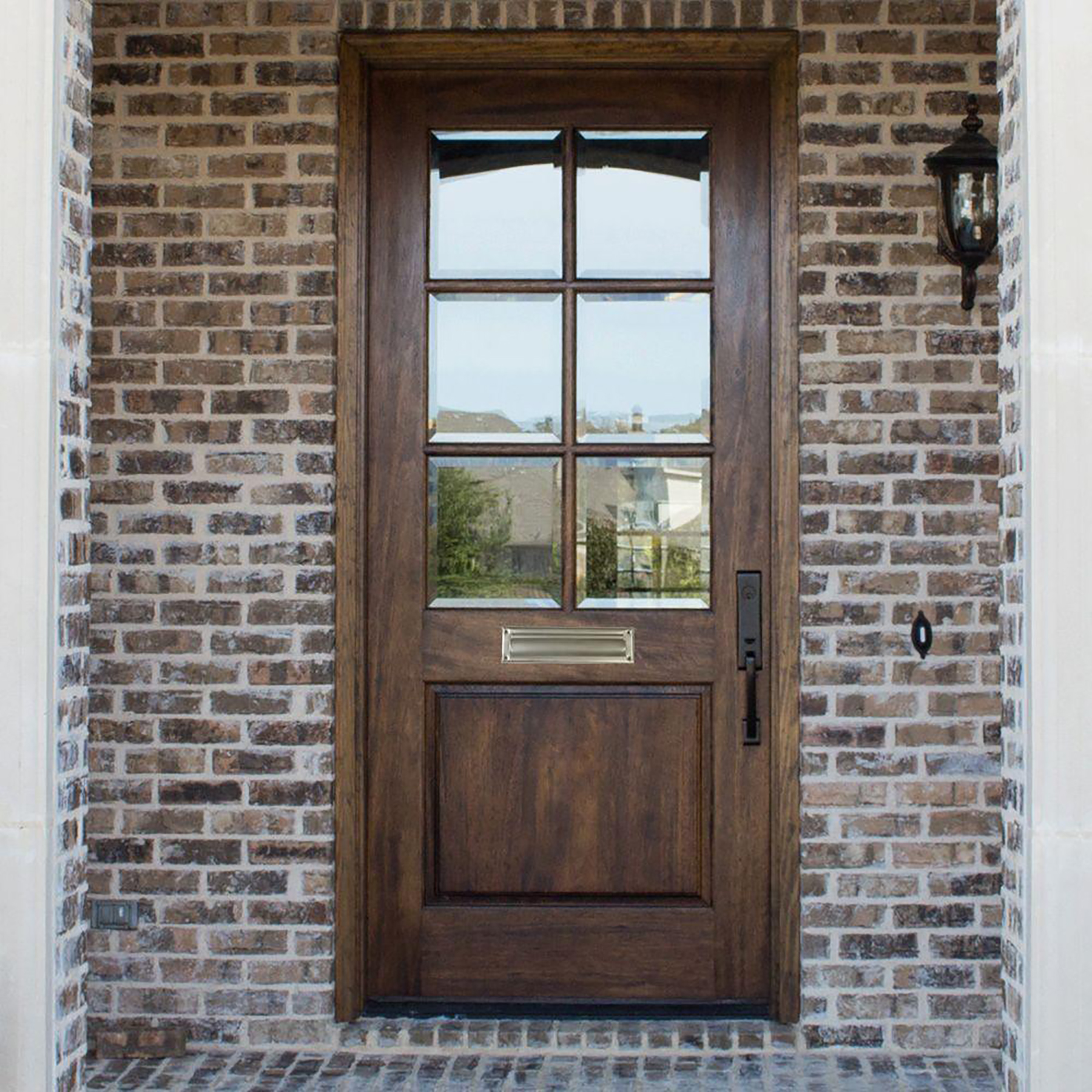 Wooden front door with a six-pane glass window set in a brick entryway, plus a black lantern on the right side.