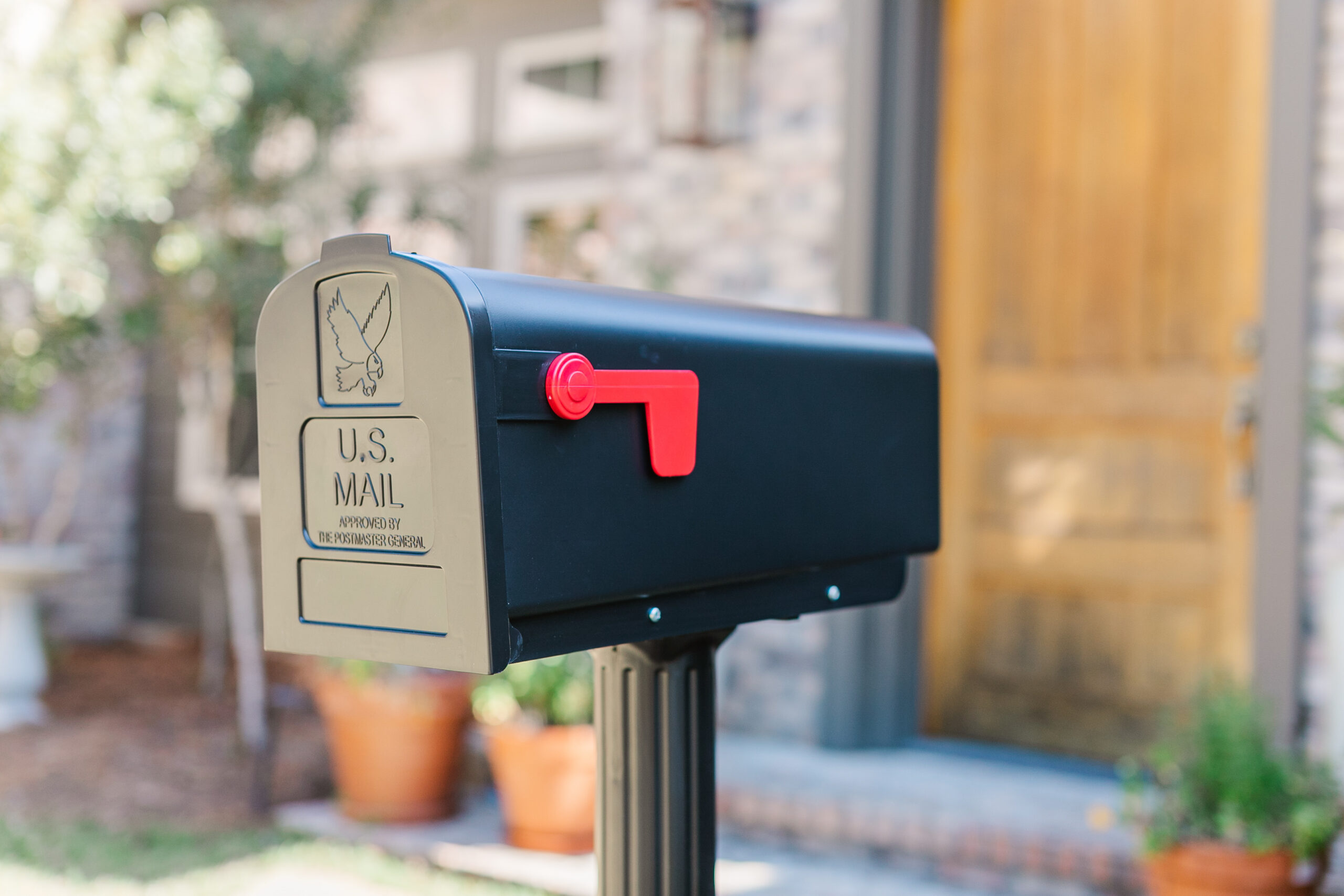 Blue U.S. Mailbox on a post in a residential front yard with the red flag raised and ready for outgoing mail.