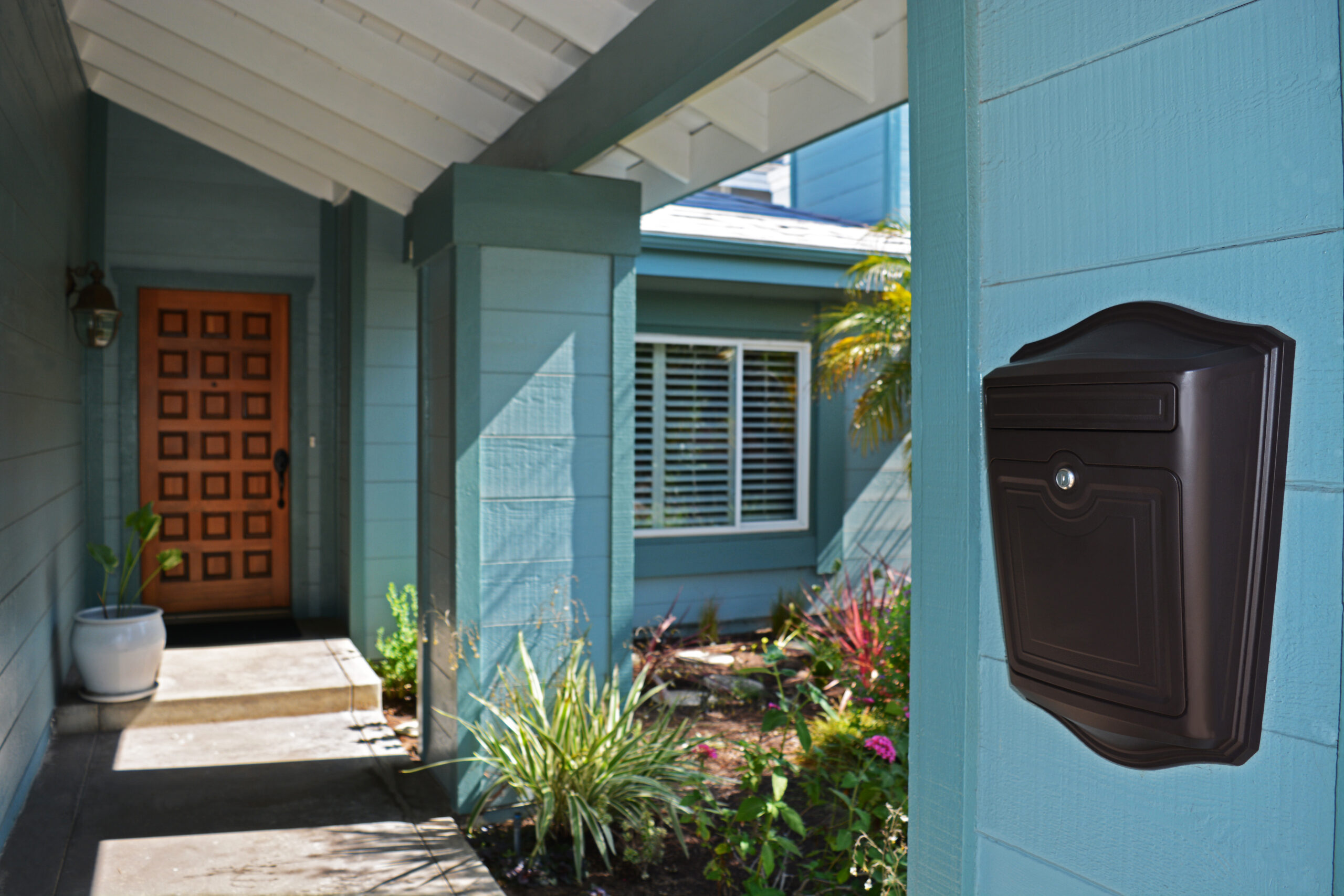 Blue suburban house exterior with a wooden front door and a black wall mailbox in the foreground.