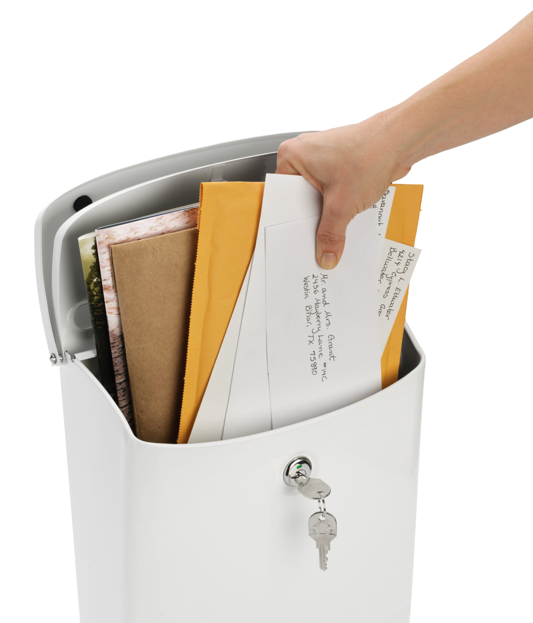 Hand placing envelopes into a white curbside mailbox with a lock and keys on the front.