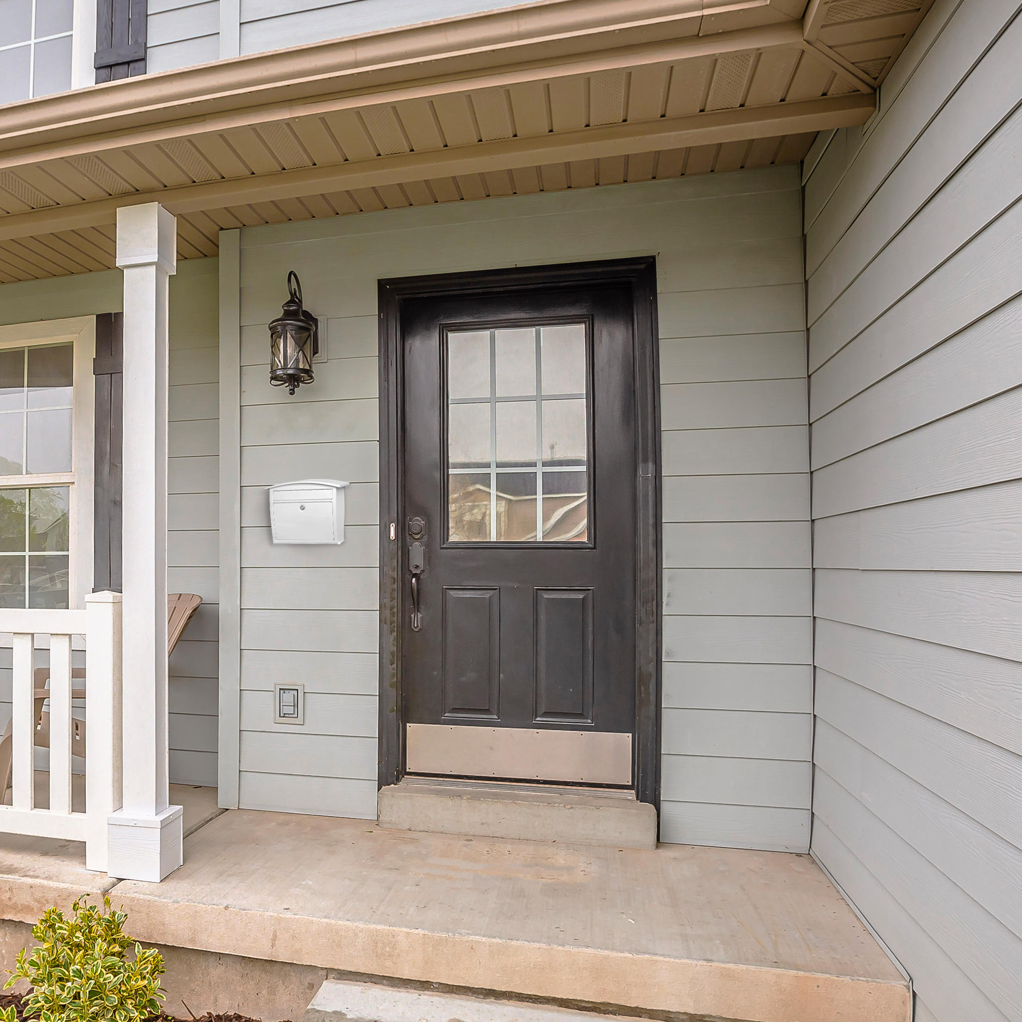 Black front door with window panes, gray siding, and a white mailbox on the left—entry to a suburban home with a lantern light above the door.