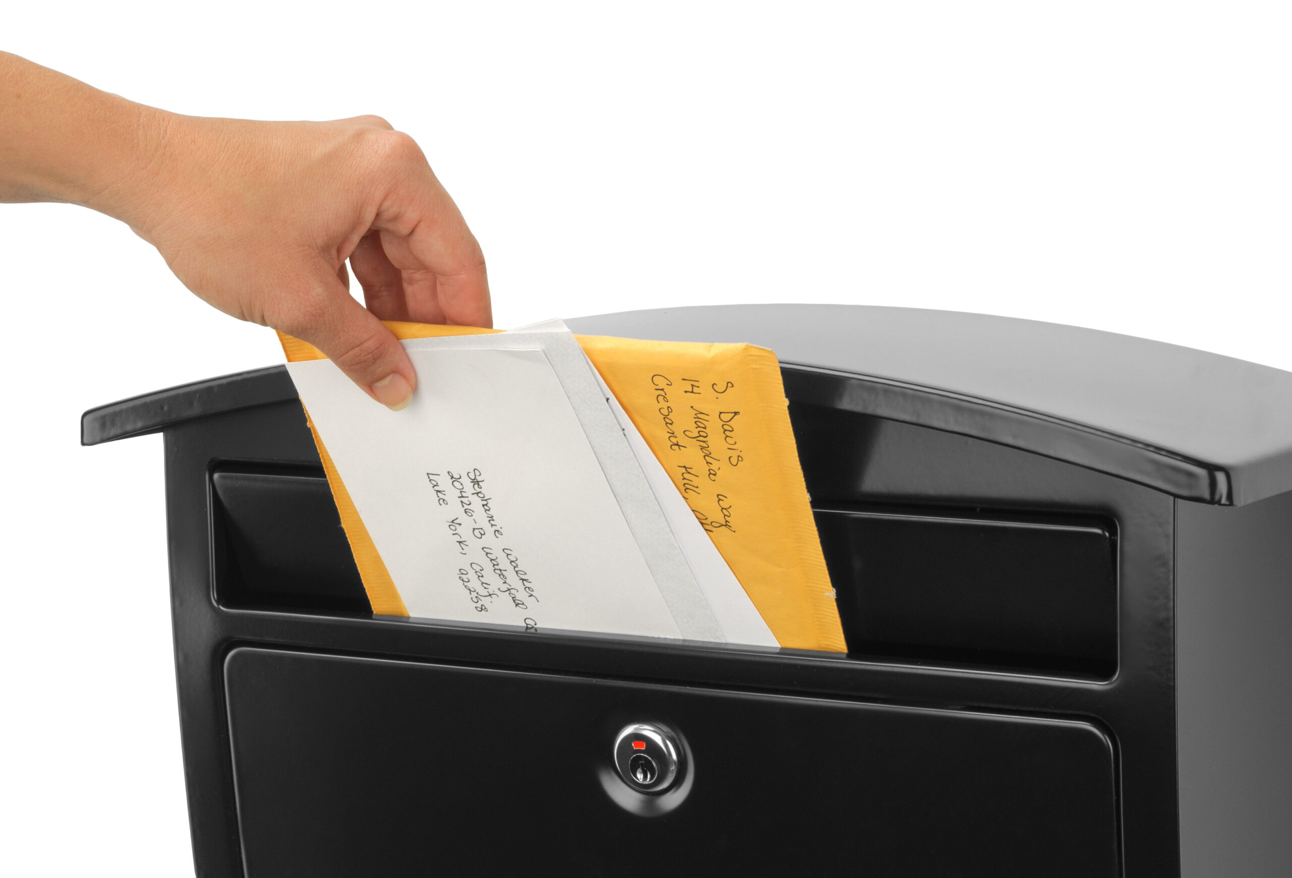 Person dropping a letter into a black mailbox slot, envelope partially visible.