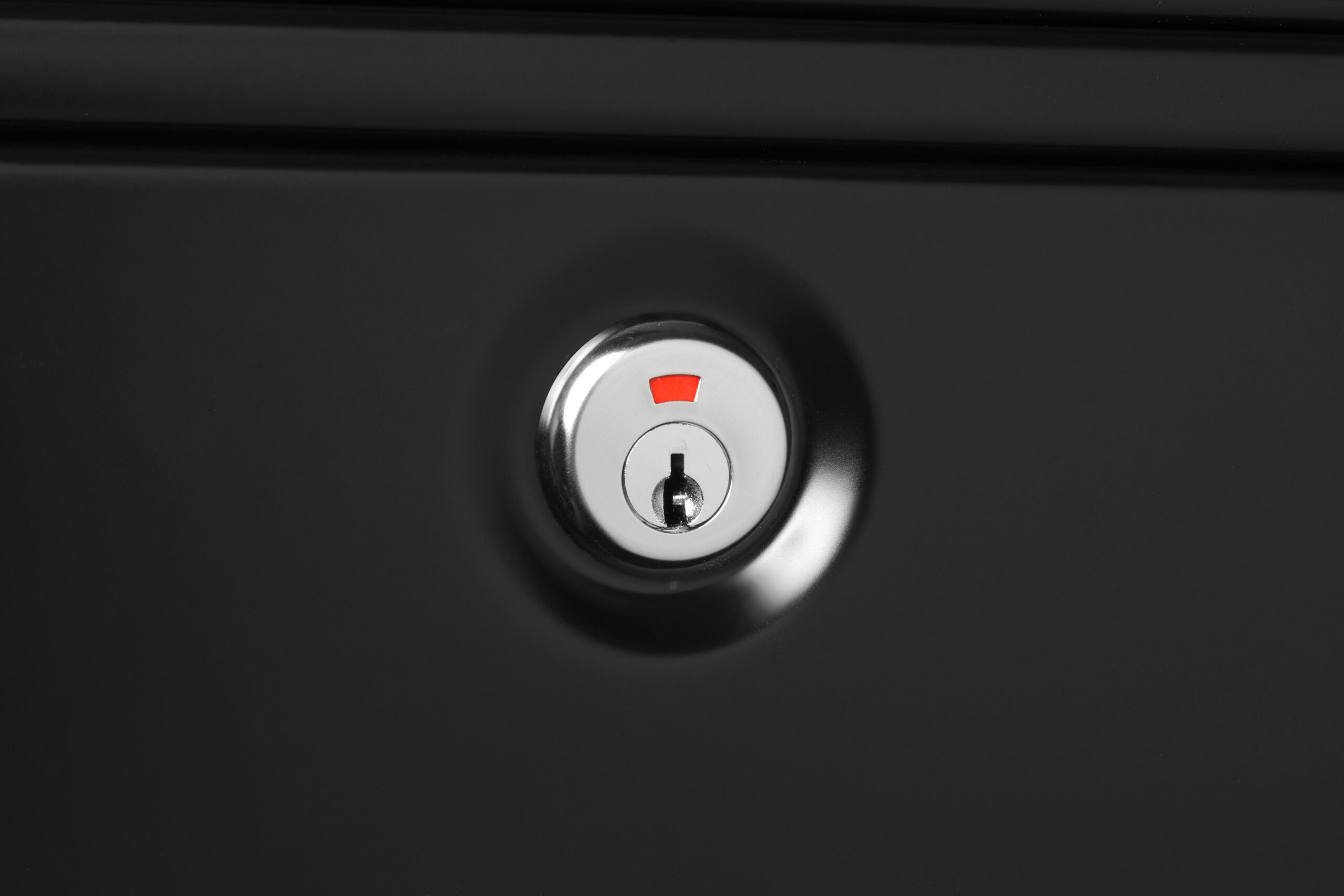 Close-up of a metallic door lock with a red indicator on a dark door surface.