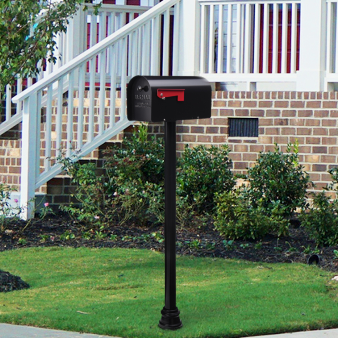Black USPS-style mailbox with red flag on a tall black post in a landscaped front yard by a brick house with stairs and shrubs nearby.