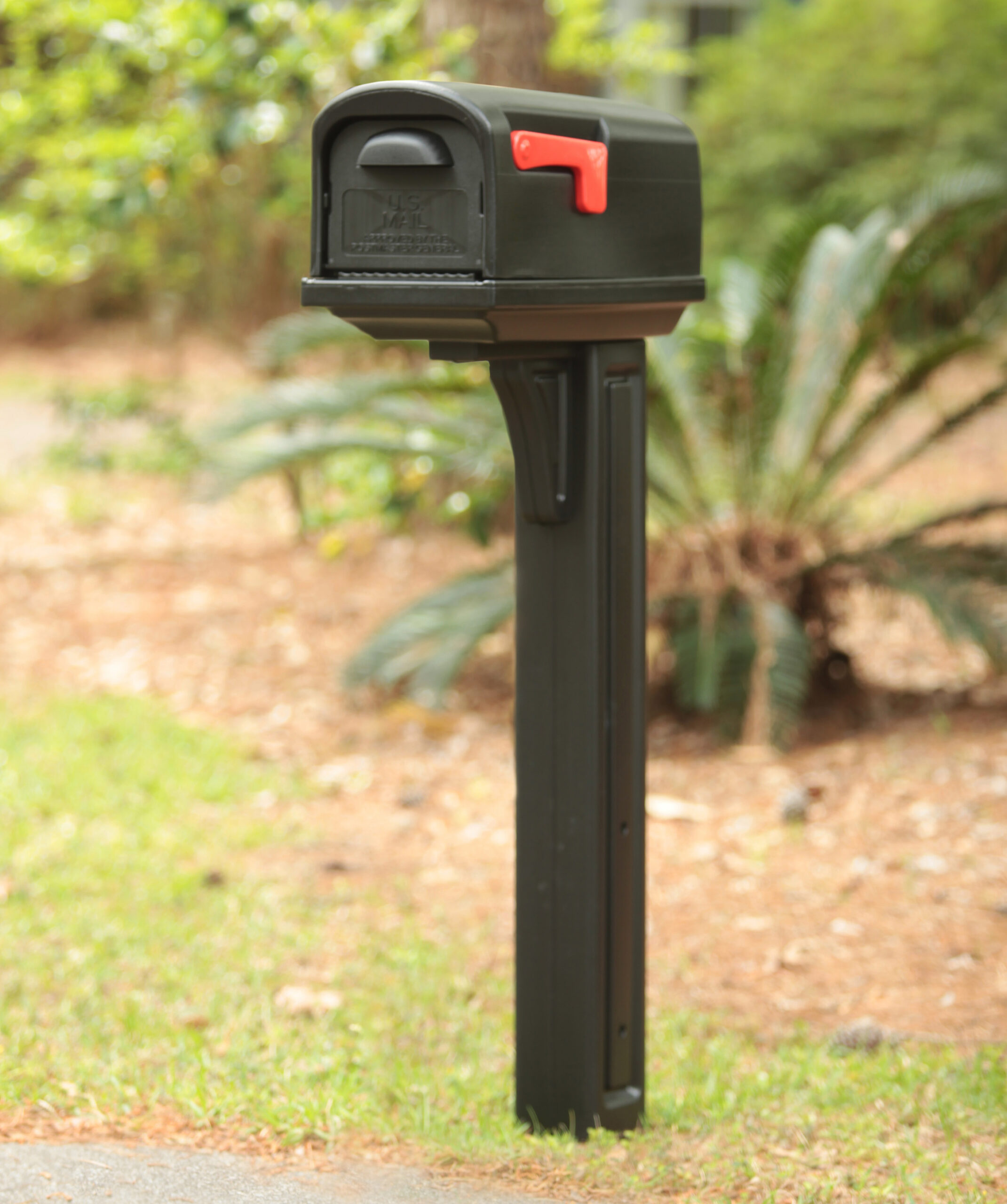 Black mailbox with a red flag mounted on a tall post in a suburban yard.