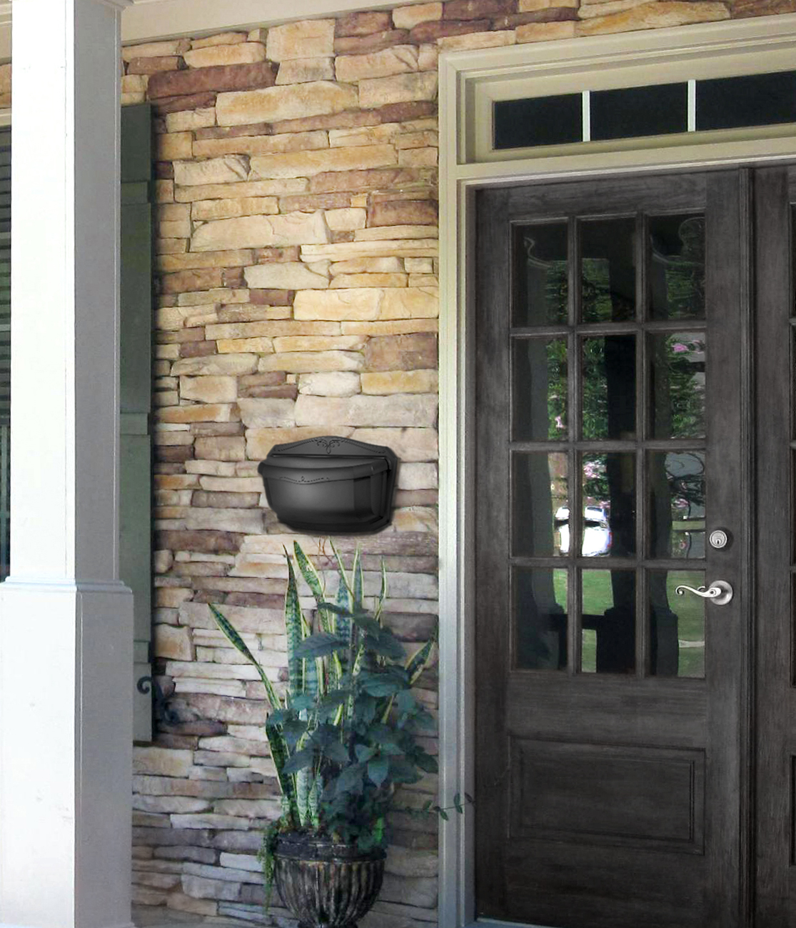 Black wall-mounted outdoor grill attached to a stone porch wall next to a dark wooden door, with a potted plant nearby.