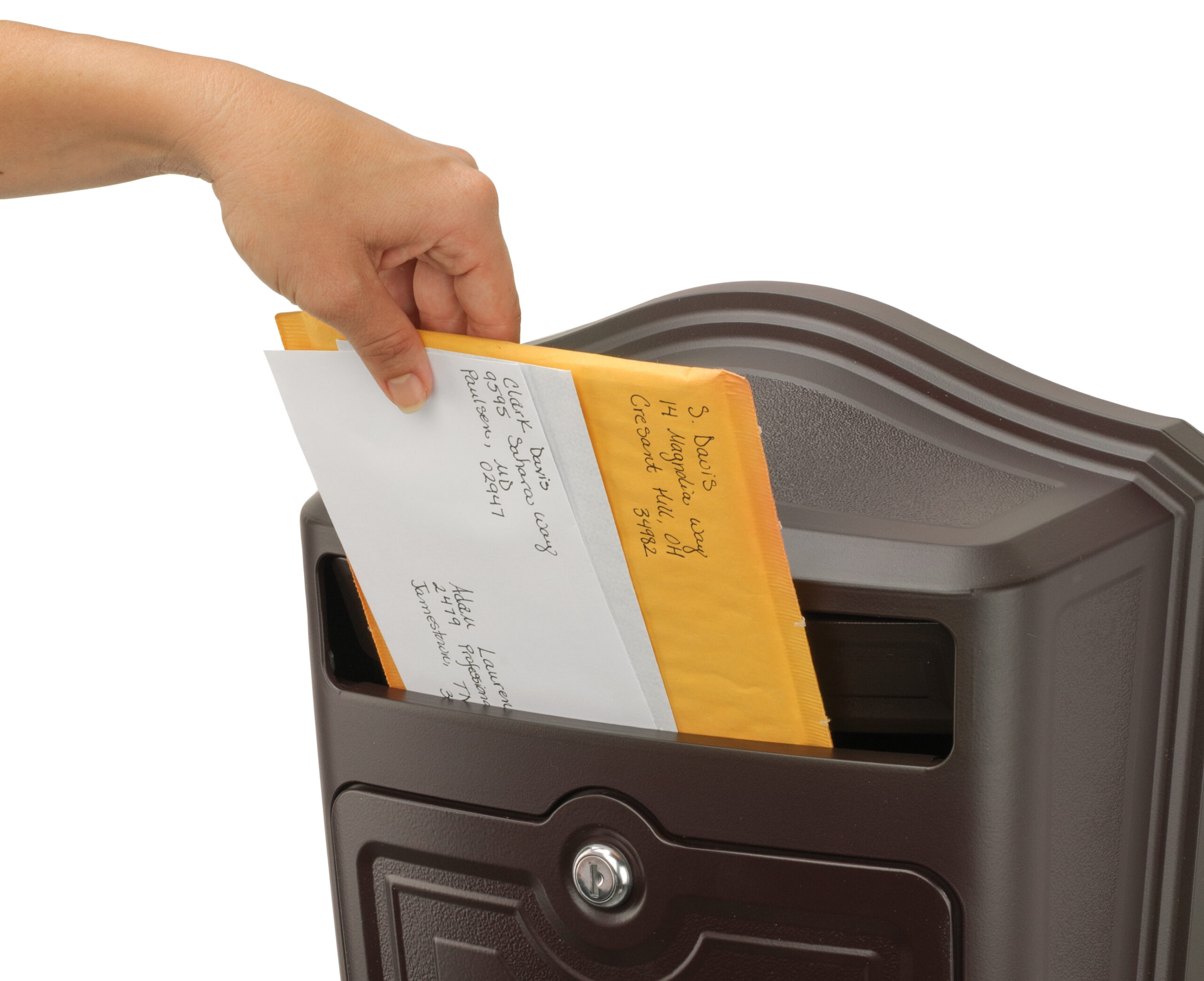 Person's hand inserting a white envelope with a yellow padded mailer into a dark mailbox slot.