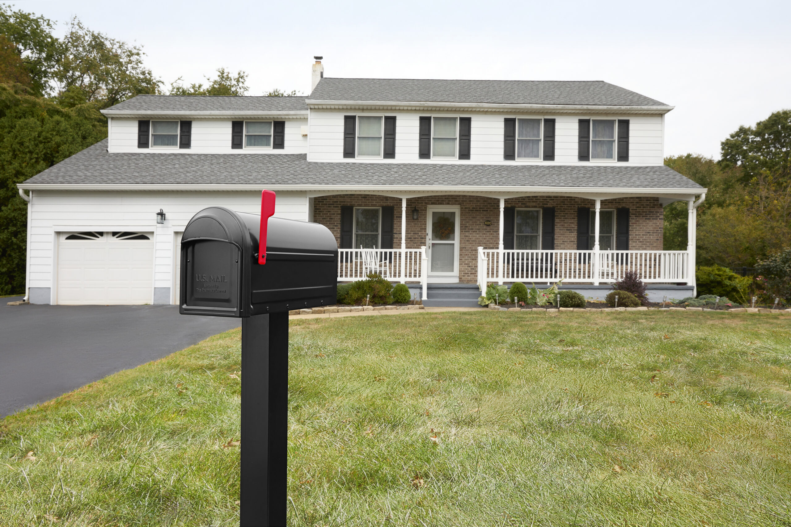 Front view of a two-story suburban house with a black mailbox on a post in the foreground and a brick porch across the front.
