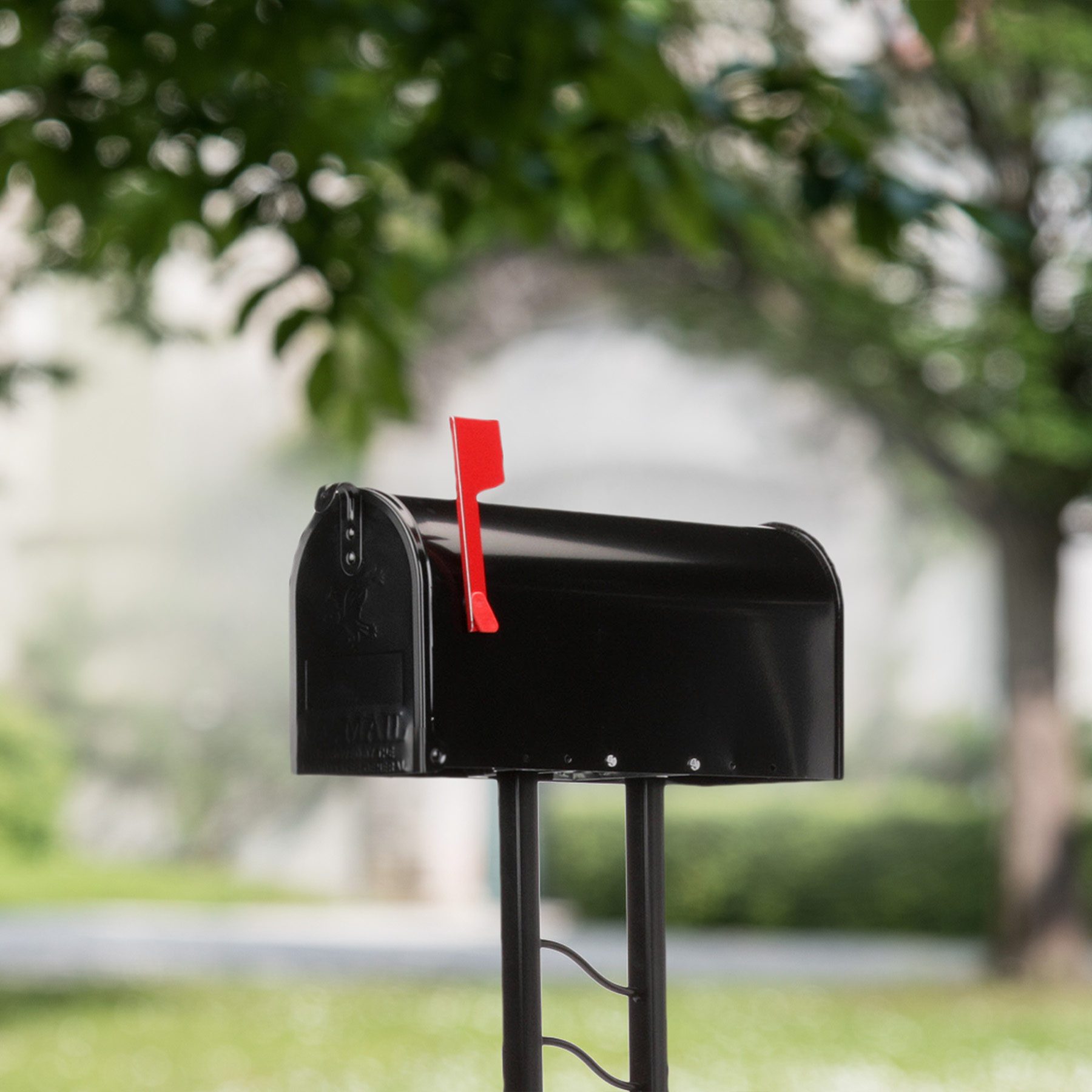 Black mailbox with a raised red flag mounted on a metal post in a green, suburban yard