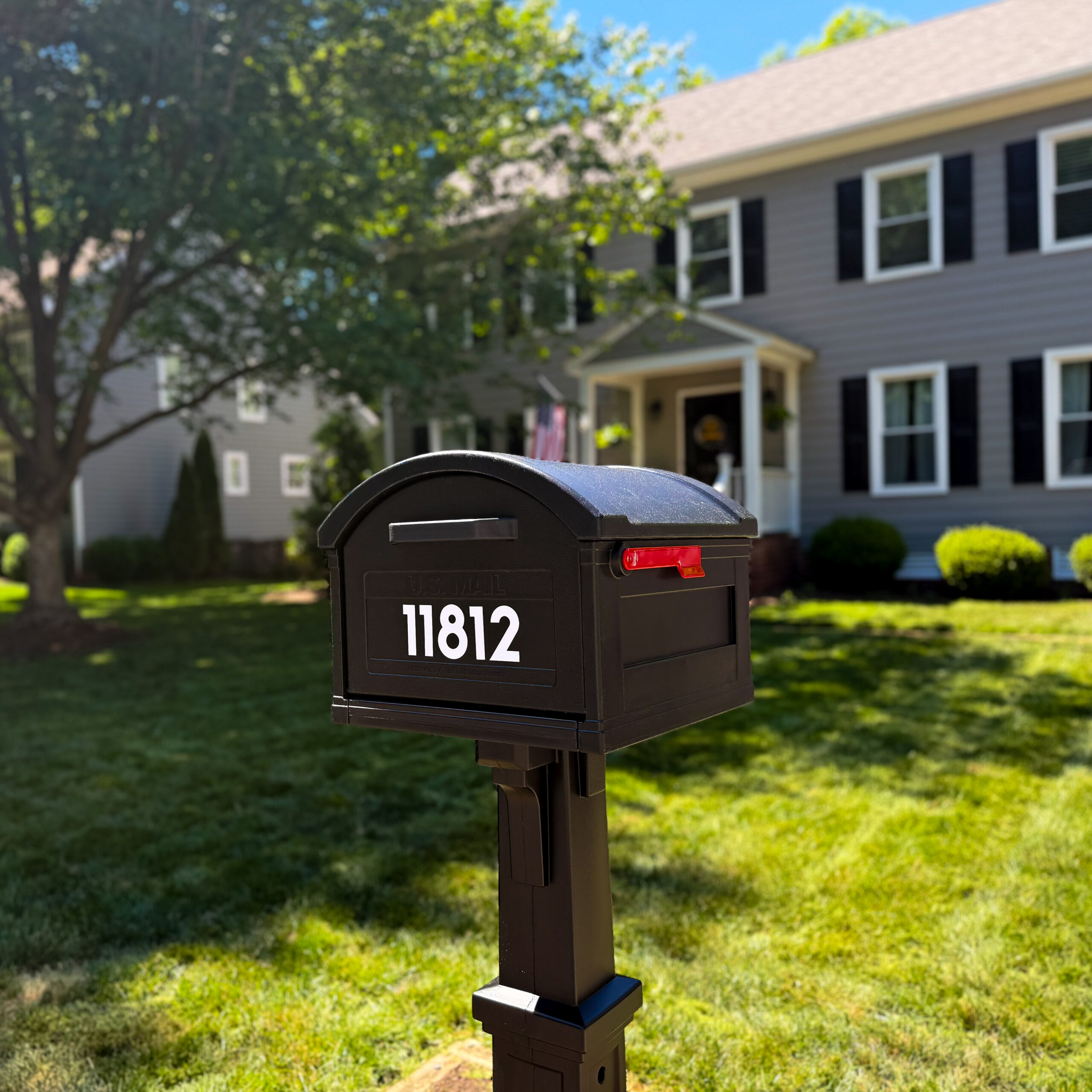 Black mailbox on a post in a front yard, with a gray two-story house, white trim, and black shutters in the background.