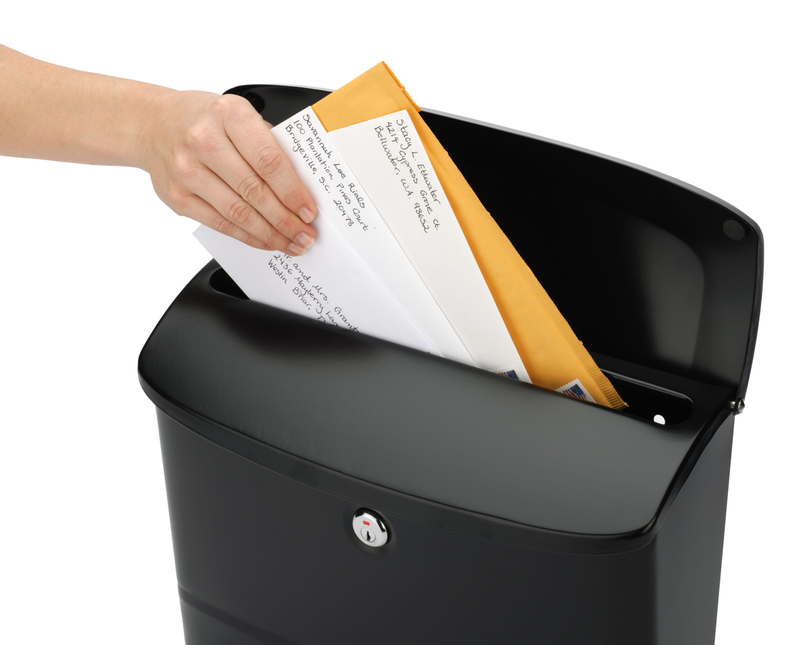 Hand placing envelopes into a black mailbox with a slot.