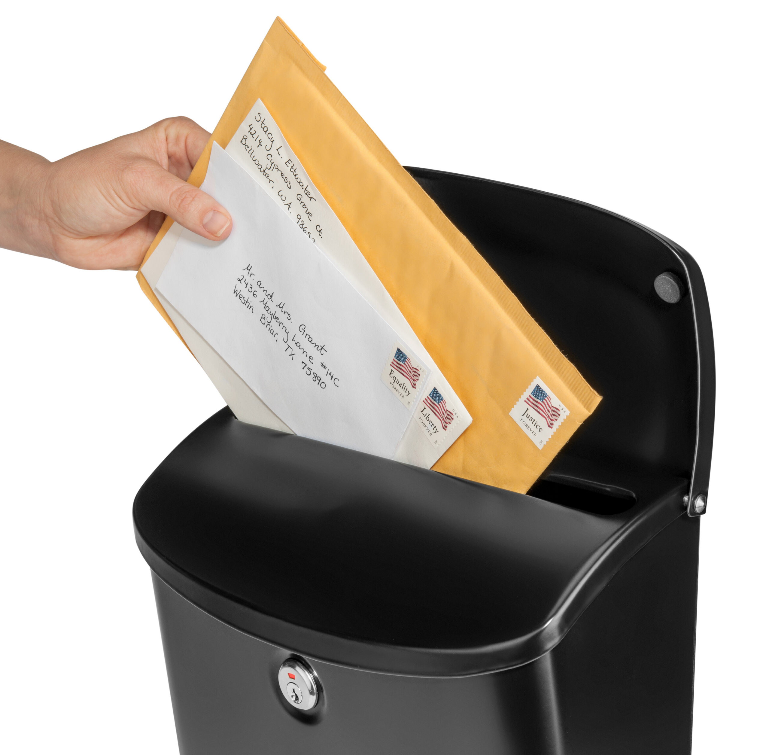 Person dropping an envelope with stamps into a black mailbox