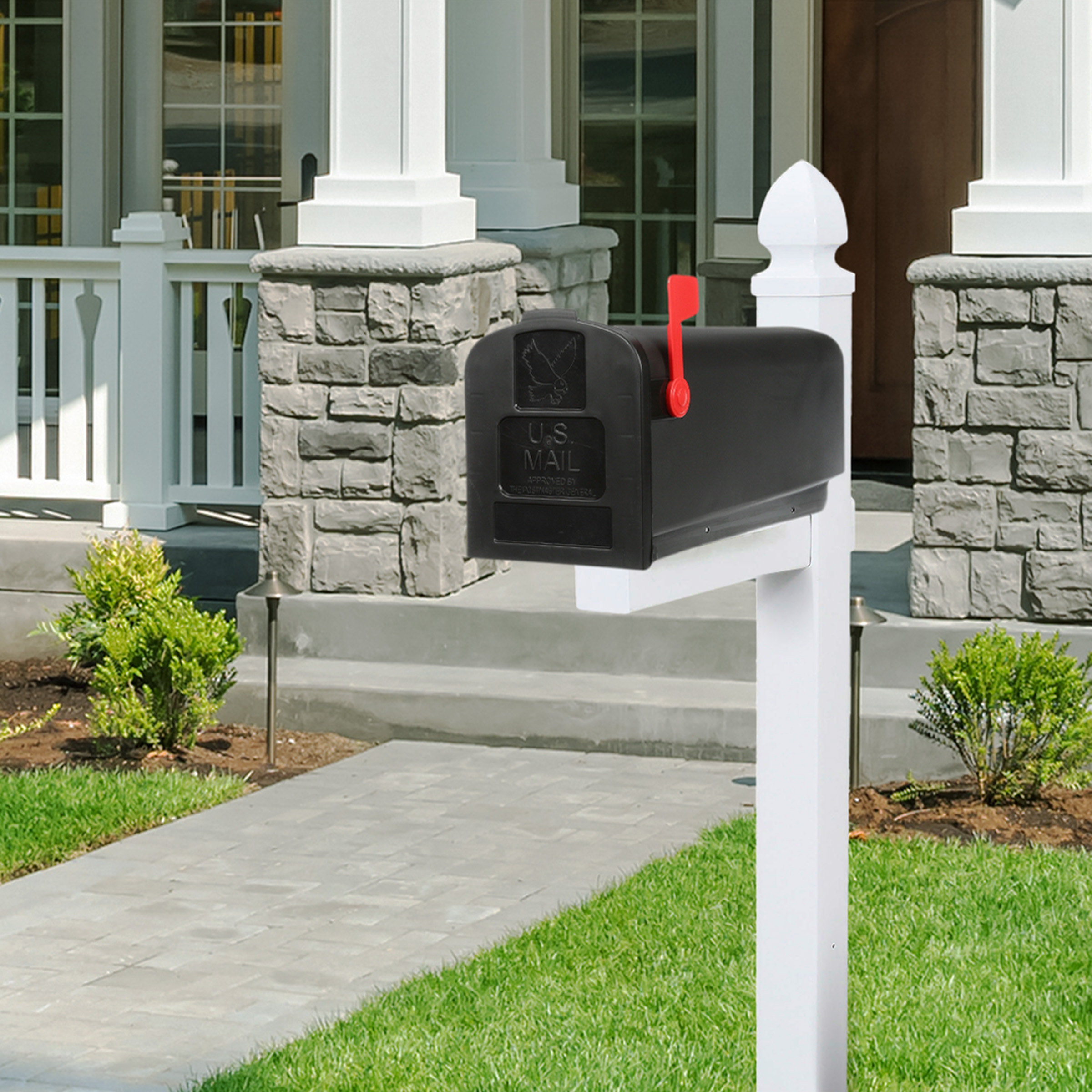 Black U.S. Mail mailbox with red flag raised on a white post in a suburban front yard.