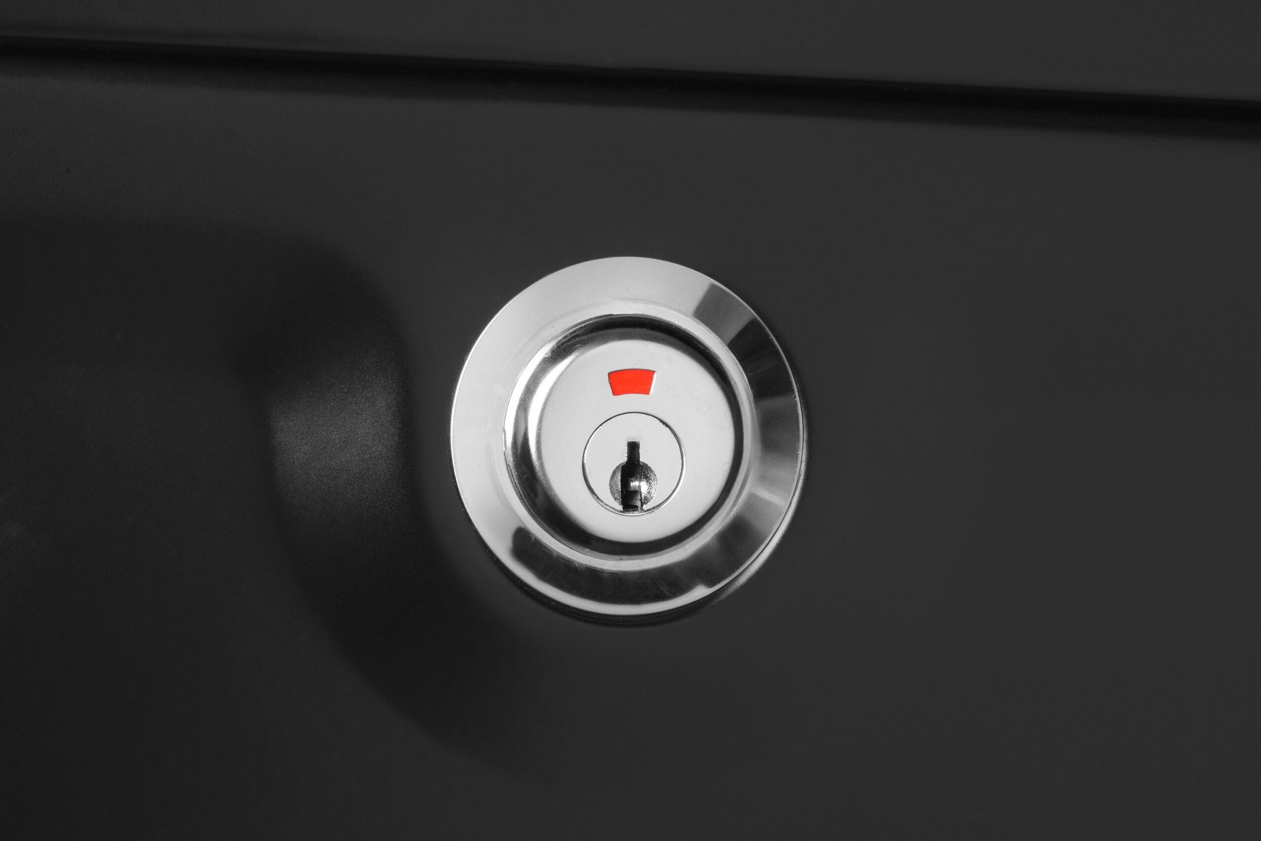 Close-up of a silver door lock cylinder with a red indicator on a dark door—conveys locked entry hardware.
