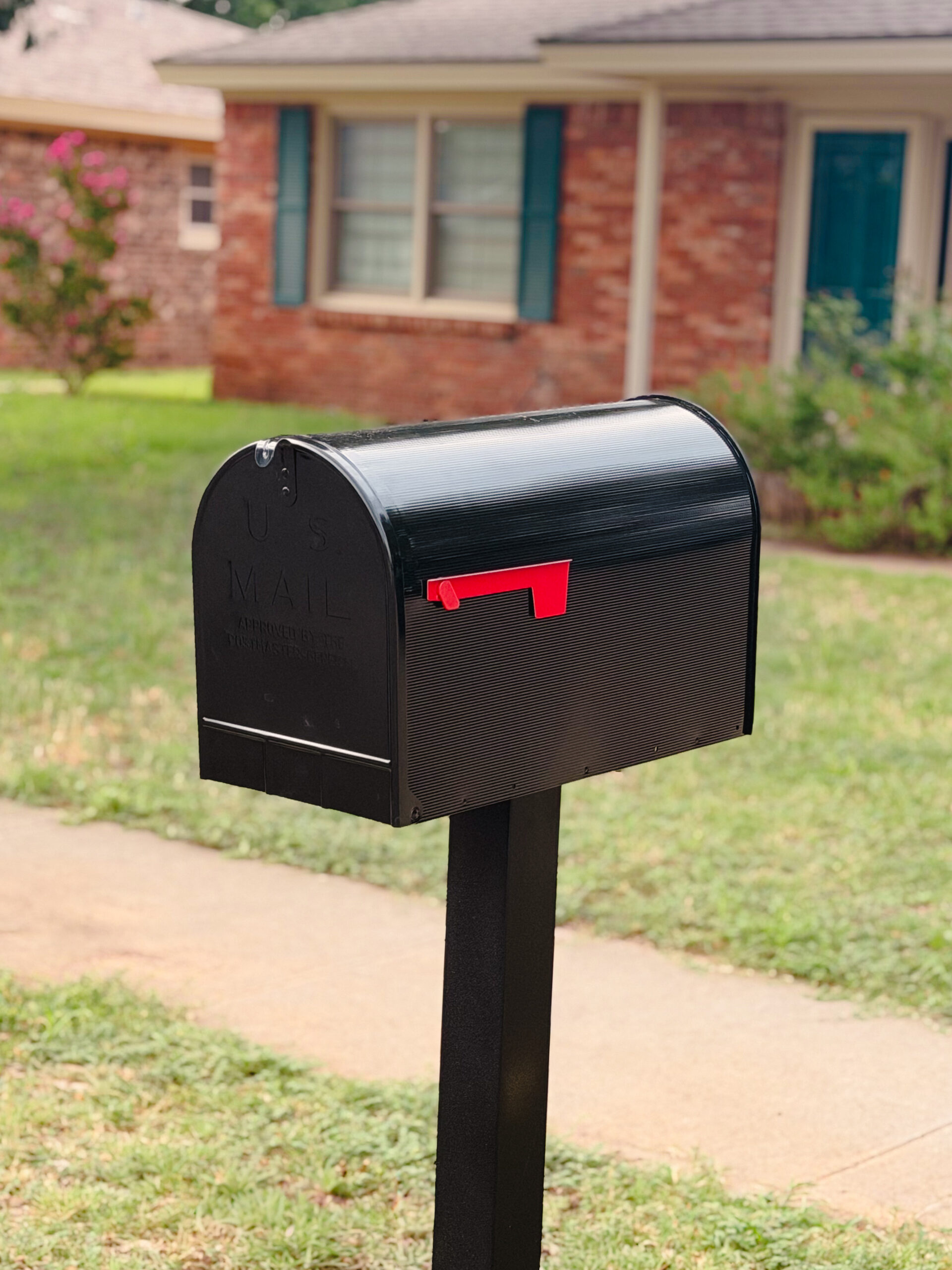 Black metal mailbox with a red flag on a post in a suburban front yard.