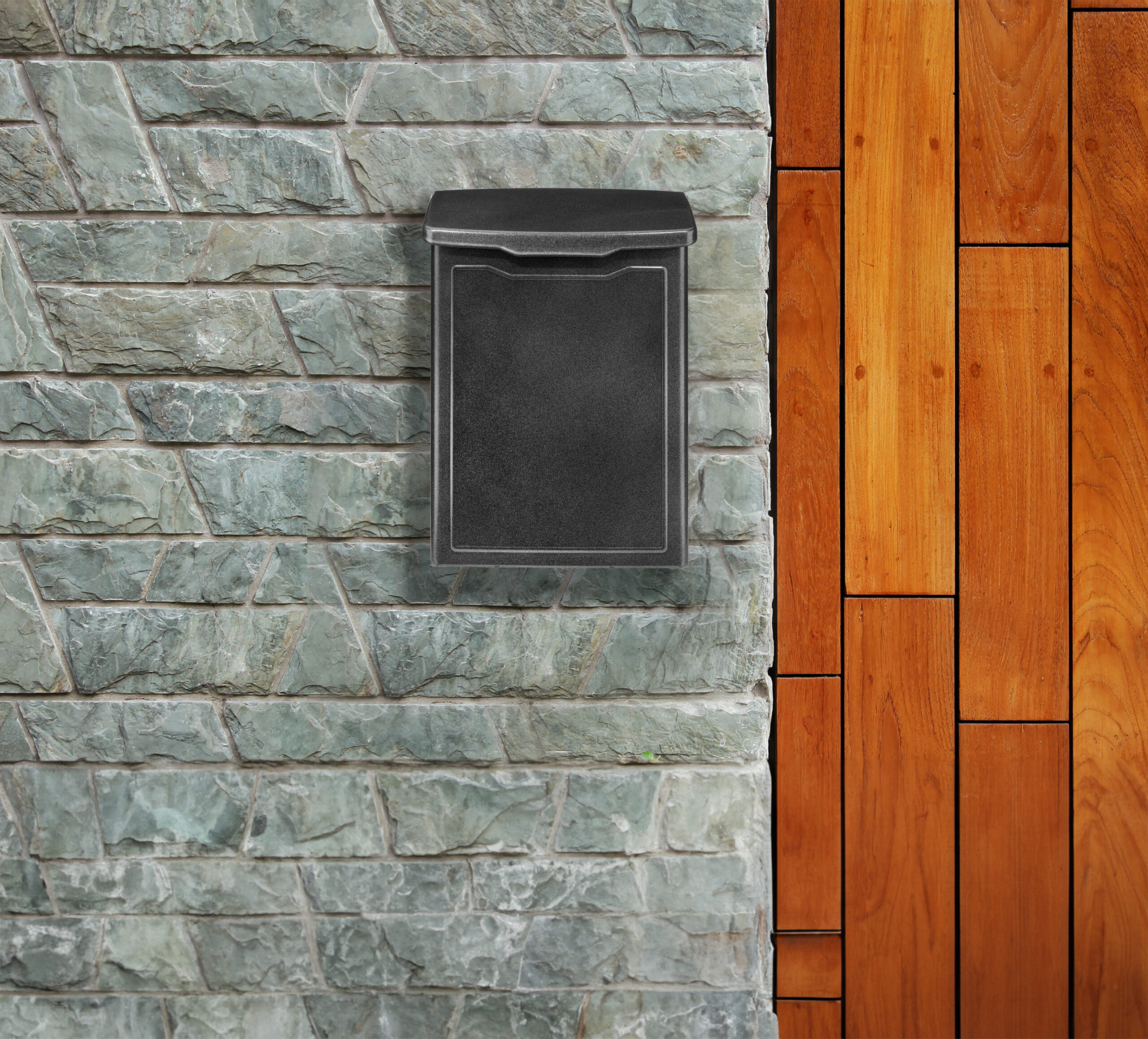 Black metal wall-mounted mailbox on a gray stone wall beside a wooden deck.