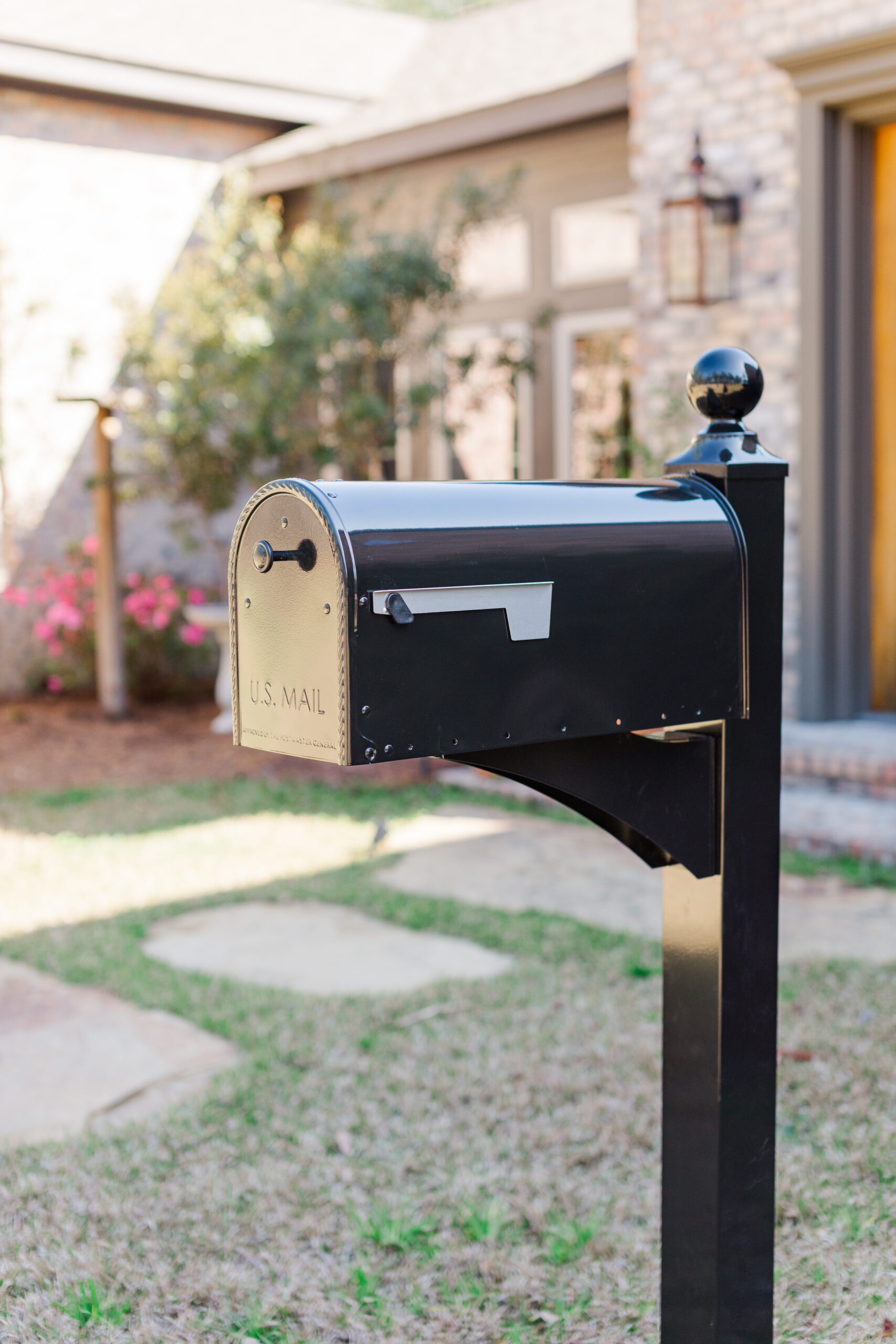 Black mailbox labeled U.S. Mail on a post in a front yard with a brick house in the background