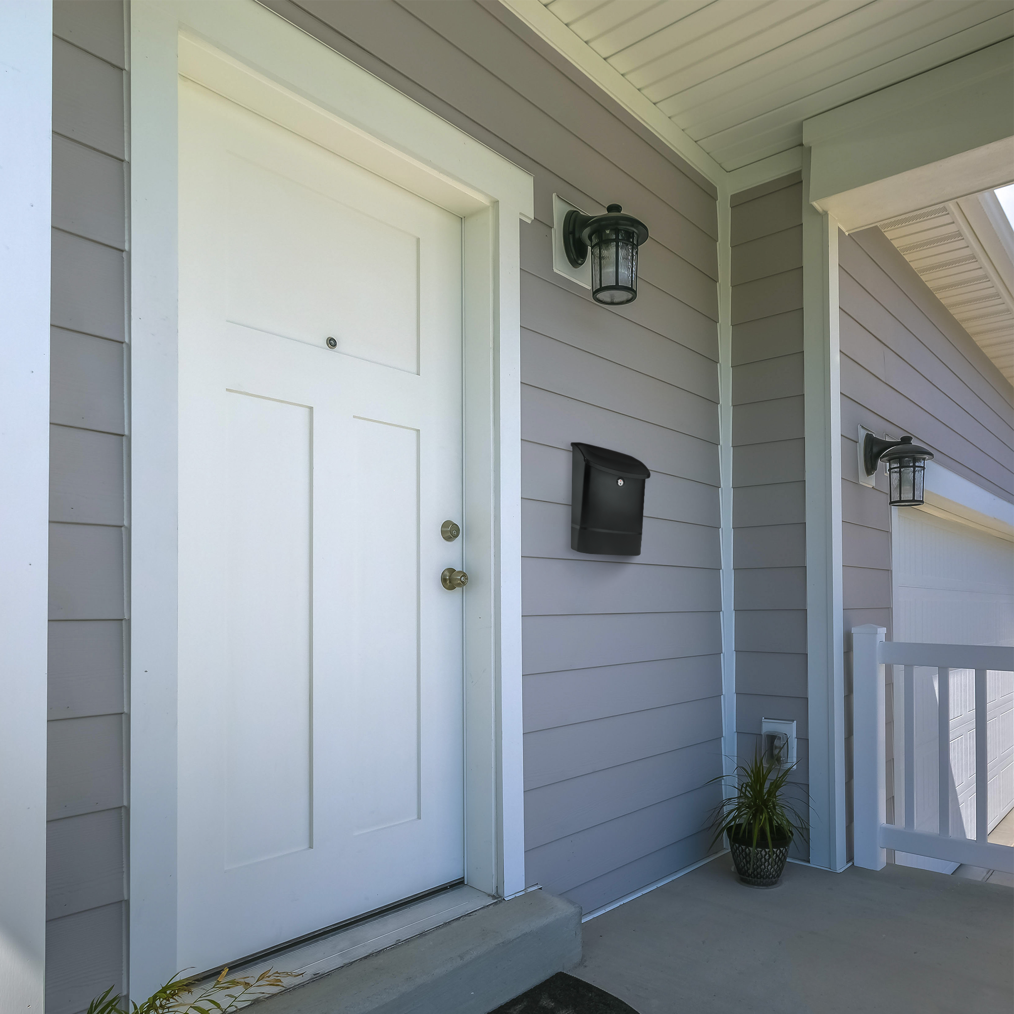 White front door with peephole set in gray siding, a black wall mailbox mounted to the right, and a plant on the porch next to a white railing.