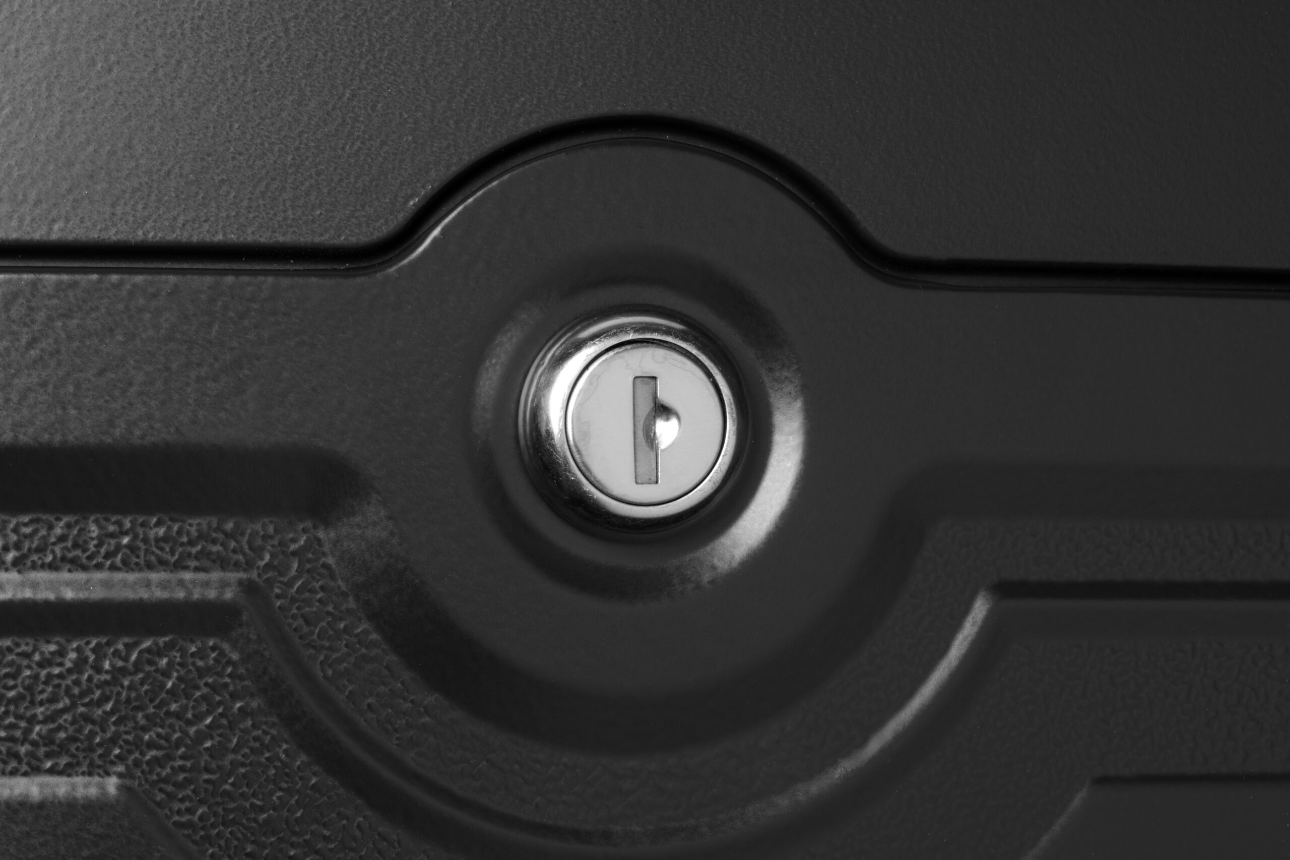 Close-up of a circular keyhole in a dark textured surface, likely a lock cylinder on a door or trunk.