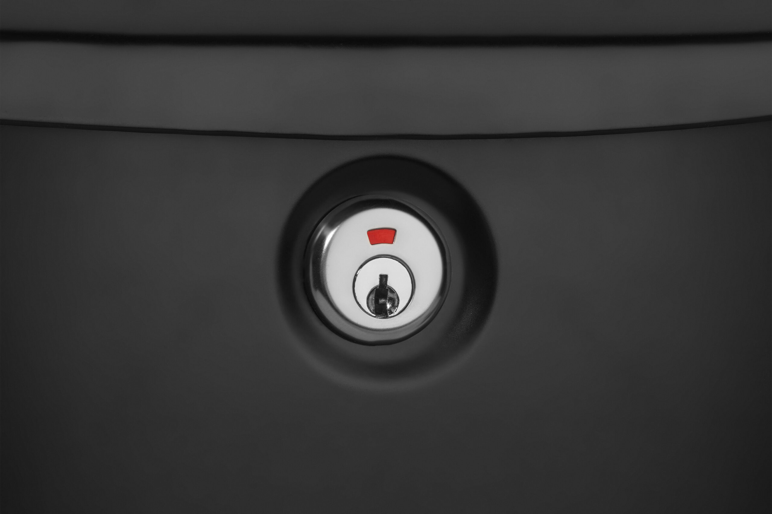 Close-up of a chrome door lock with a white surround and a small red indicator above the keyhole, set in a dark surface.