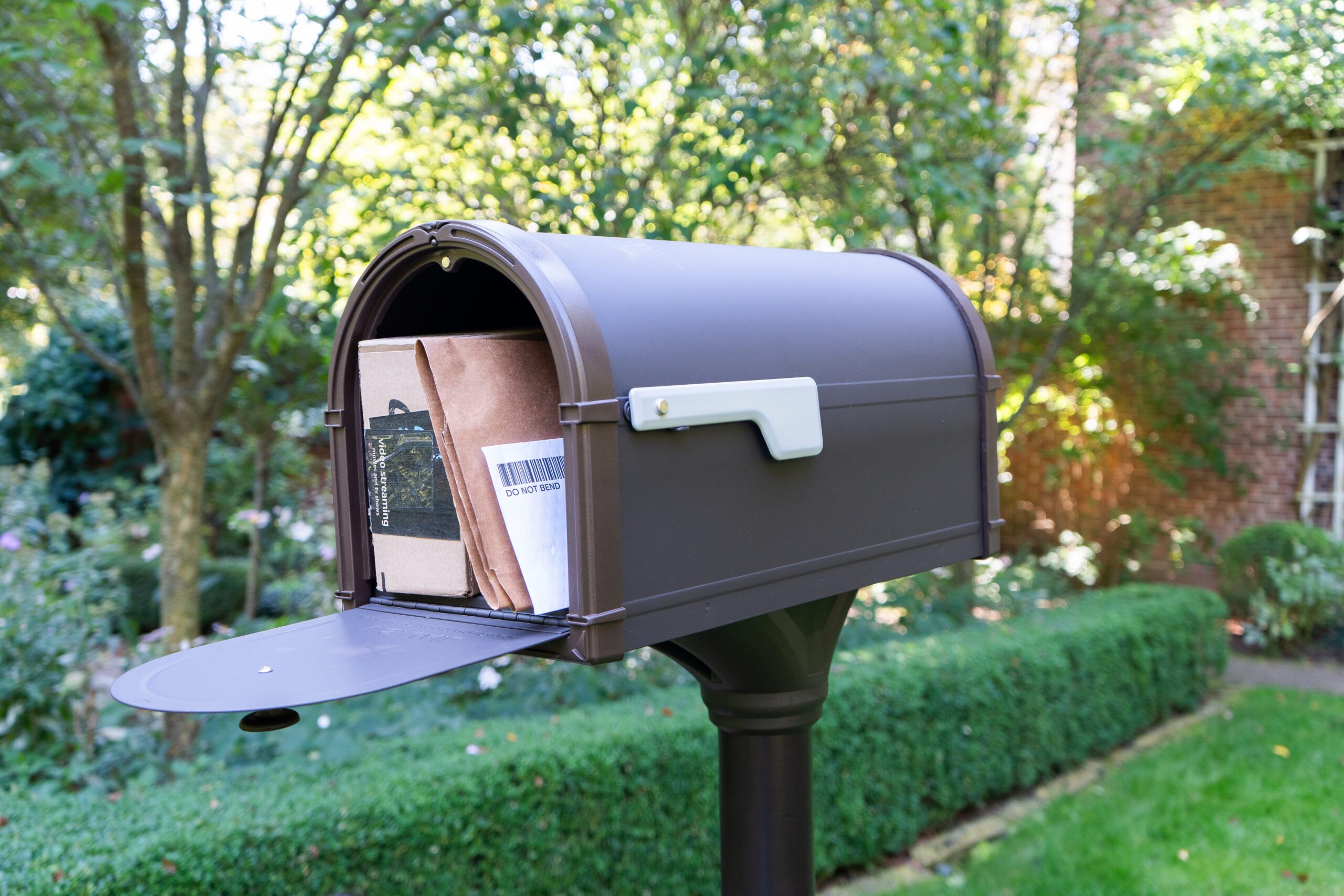 Open mailbox with cardboard packages visible inside in a green suburban yard.