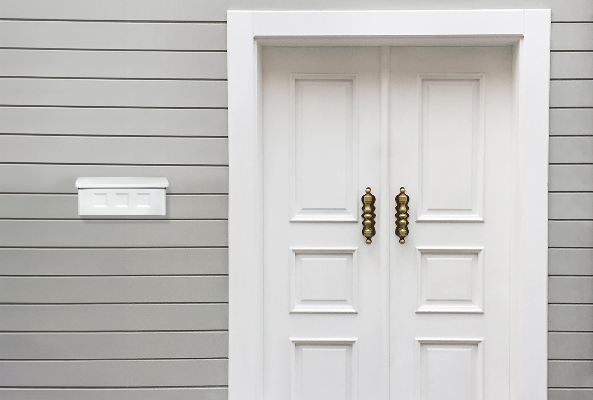 White double panel doors with ornate brass handles next to a wall mailbox on gray siding exterior.