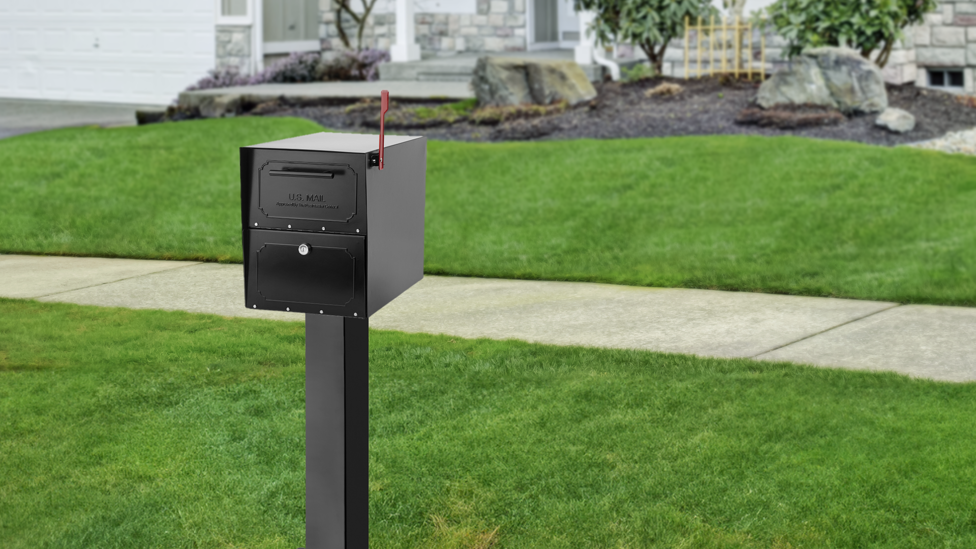 Black curbside mailbox on a tall post with a raised red flag, in a front yard near a sidewalk and suburban house.