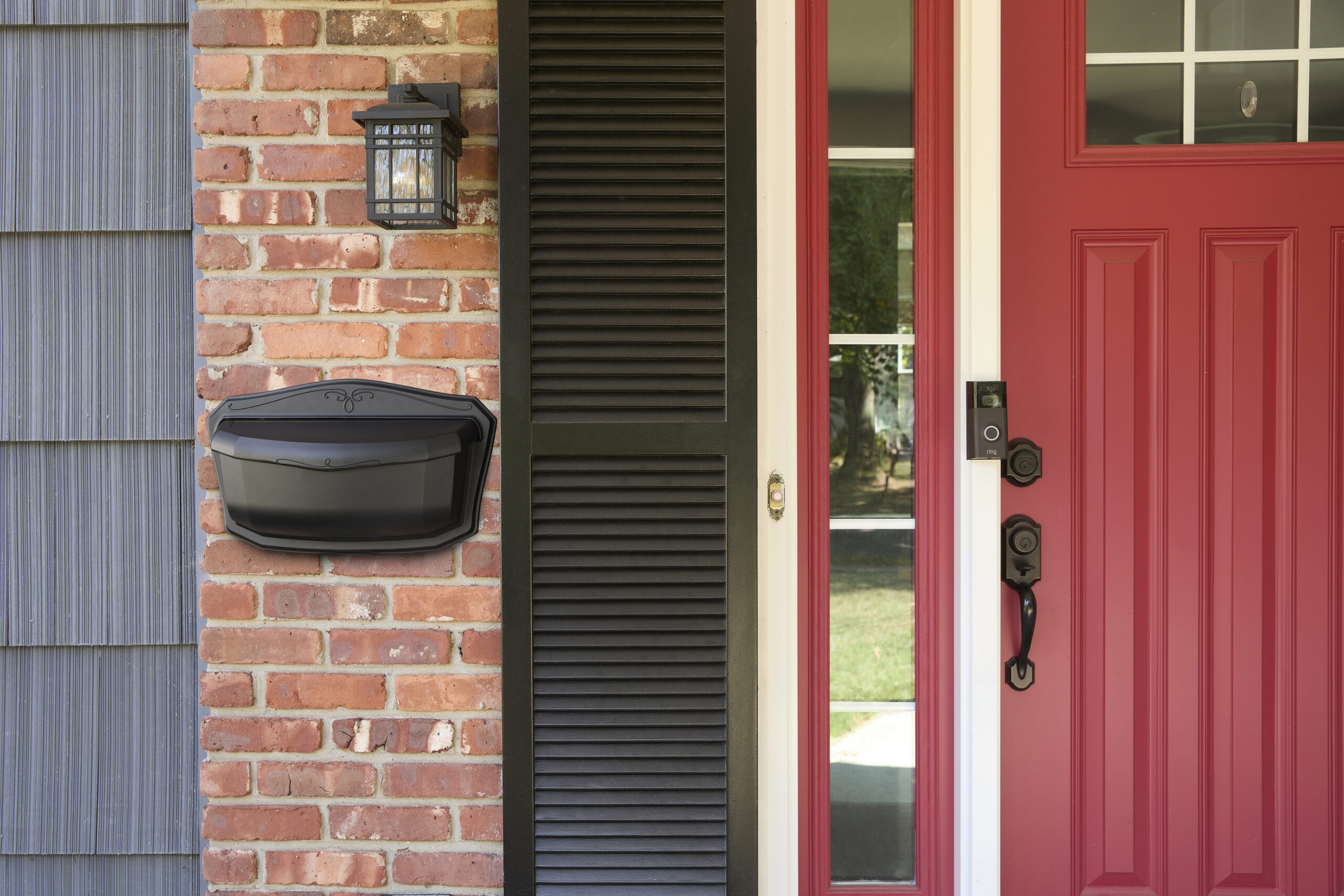 Red front door with black hardware beside a brick wall and black mailbox mounted on the brick siding.