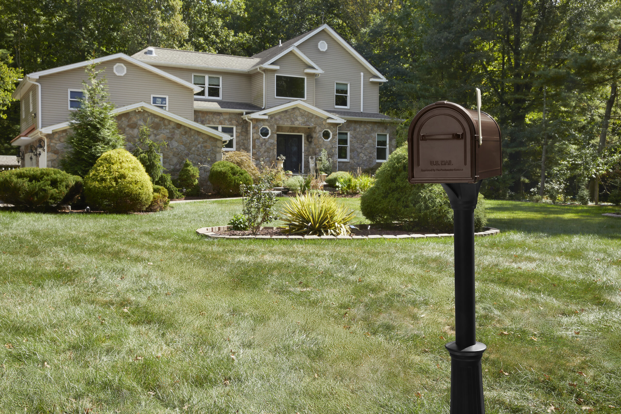 Two-story beige house with a stone facade and well-kept front yard; a brown curbside mailbox on a black post in the foreground.