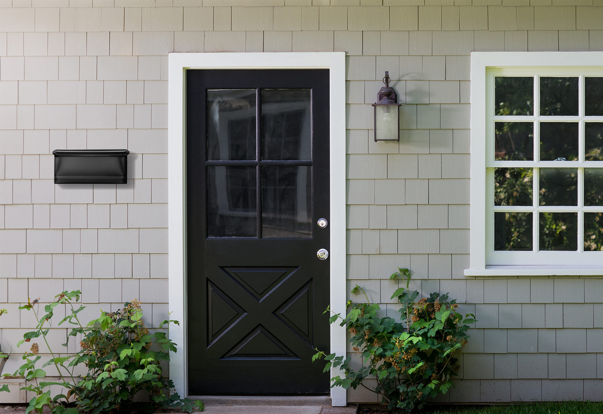 Black front door with white trim, a hanging lantern on the beige siding, and a window to the right with shrubs below. Geared for an entryway/house exterior image.