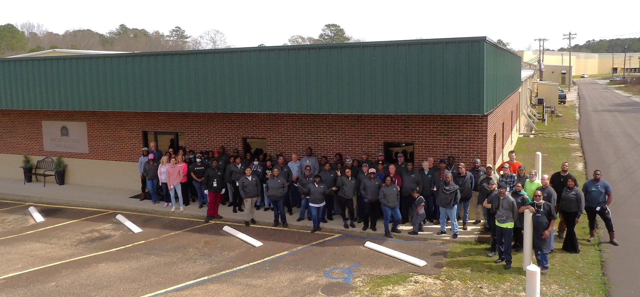 Group of people posing for a team photo outside a brick building with a green metal roof.