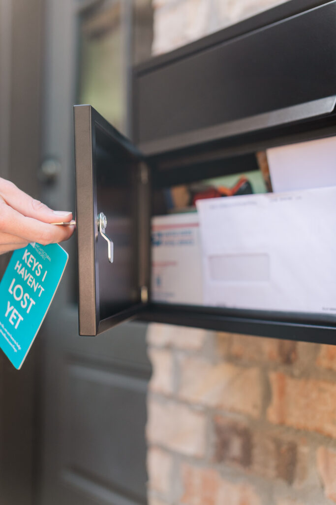 Hand placing a key into a dark metal safe or cabinet, with a turquoise tag reading 'KEYS I HAVEN'T LOST YET' visible.