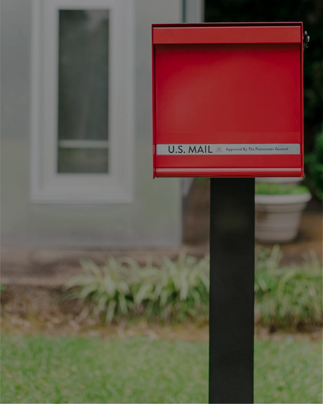 Red U.S. mailbox on a black post in a front yard; label reads 'U.S. MAIL'.