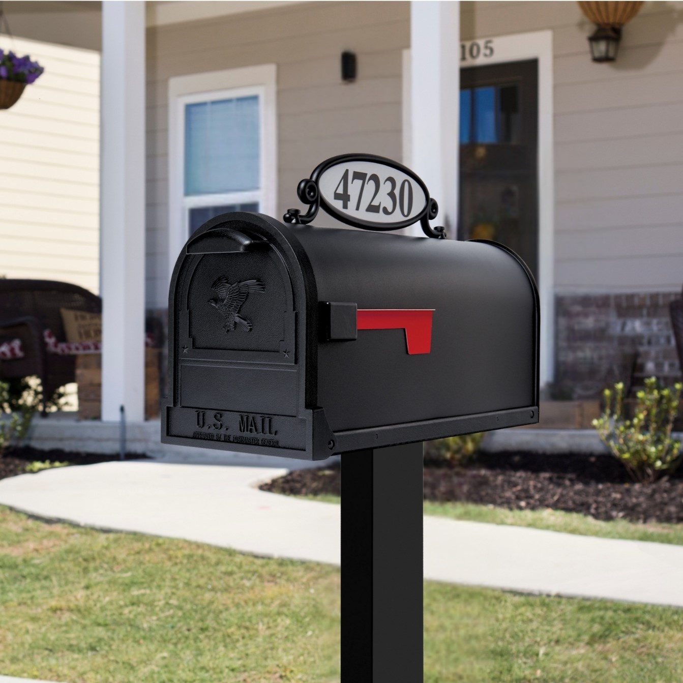 Black curbside mailbox with a raised red flag in front of a suburban house, number 47230 on the top plate.